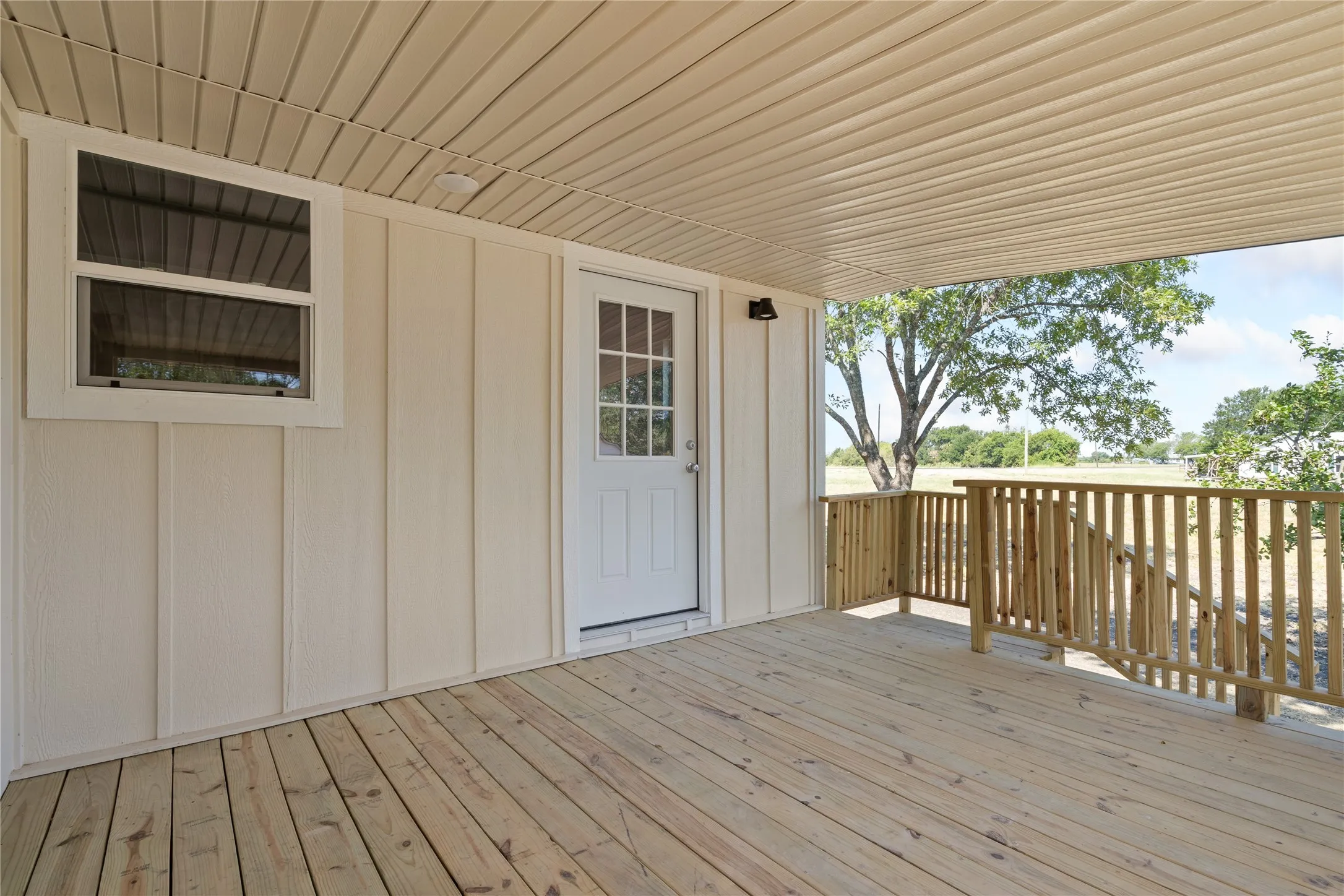 Covered porch with wood decking, wood railing, and a window with white trim