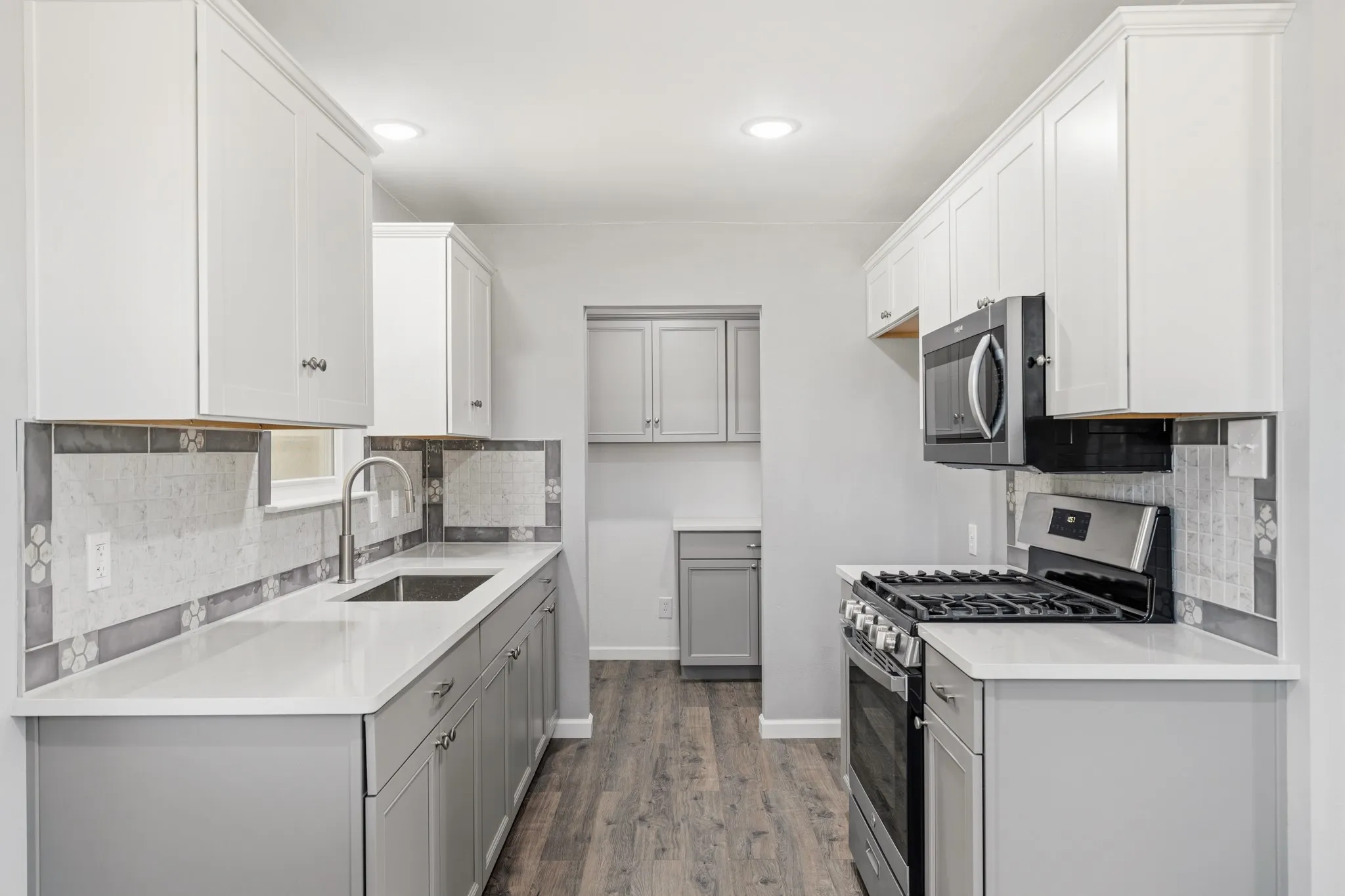 Kitchen featuring white upper cabinetry, gray lower cabinetry, light countertops, wood-finish flooring, and stainless steel appliances