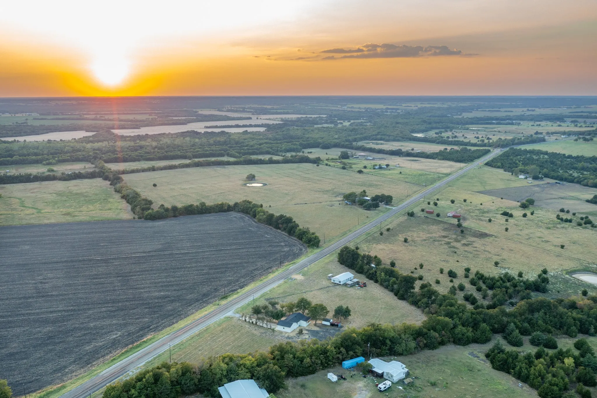 Expansive land featuring a paved road, cultivated fields, and natural water bodies