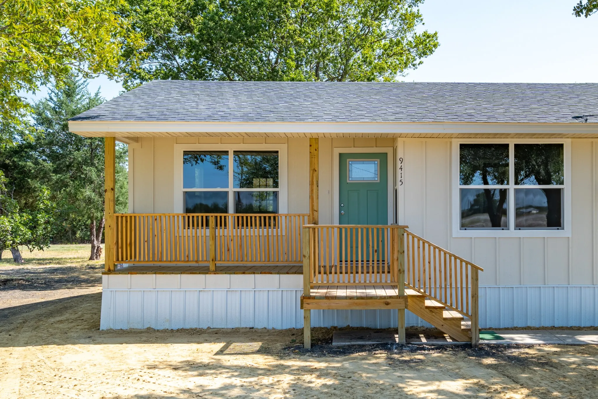 Front facade with a light-colored exterior, wood porch railing, wood porch stairs, and a teal entry door
