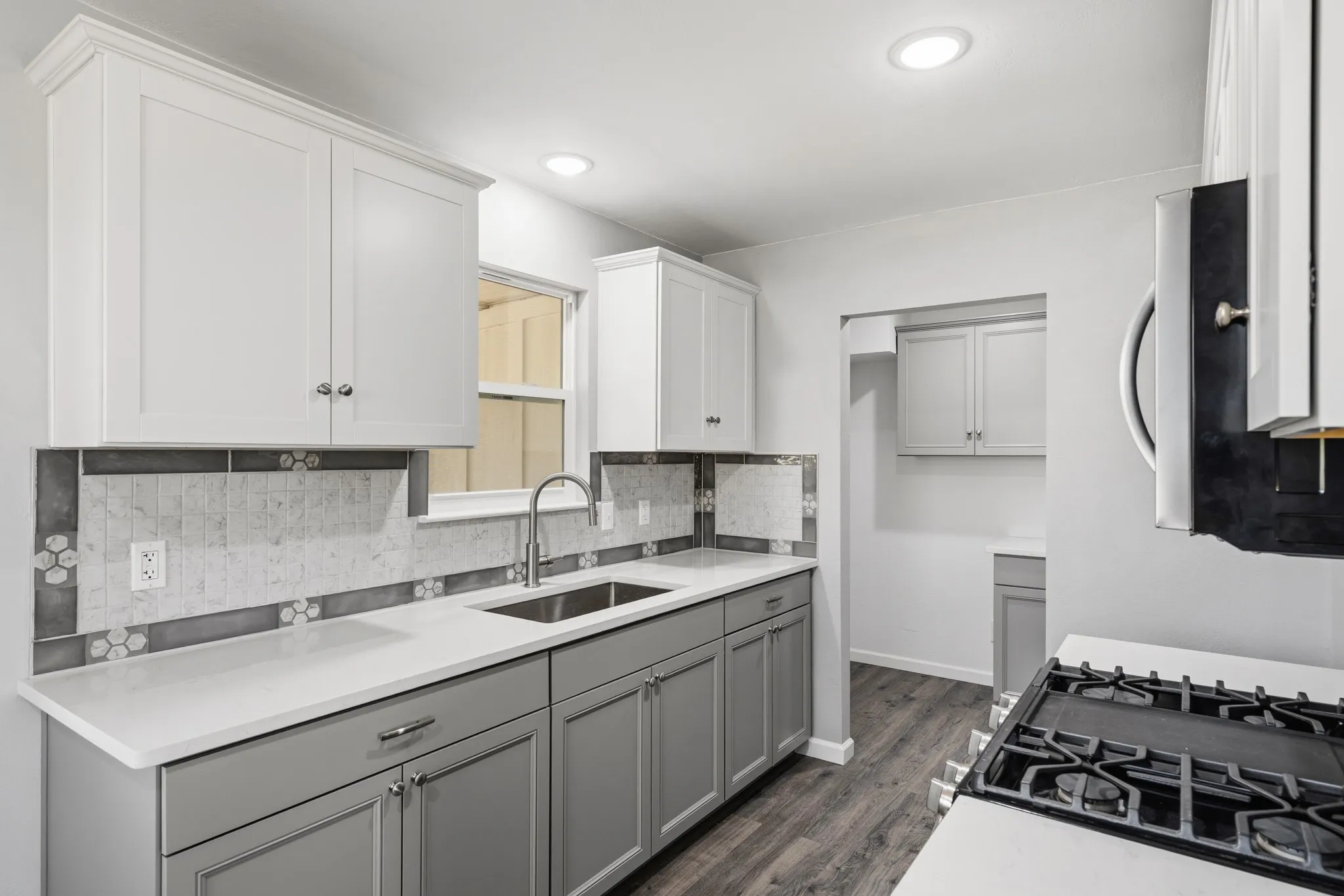Kitchen featuring two-tone cabinetry, a stainless steel sink, a gas range, recessed lighting, and wood-finish flooring