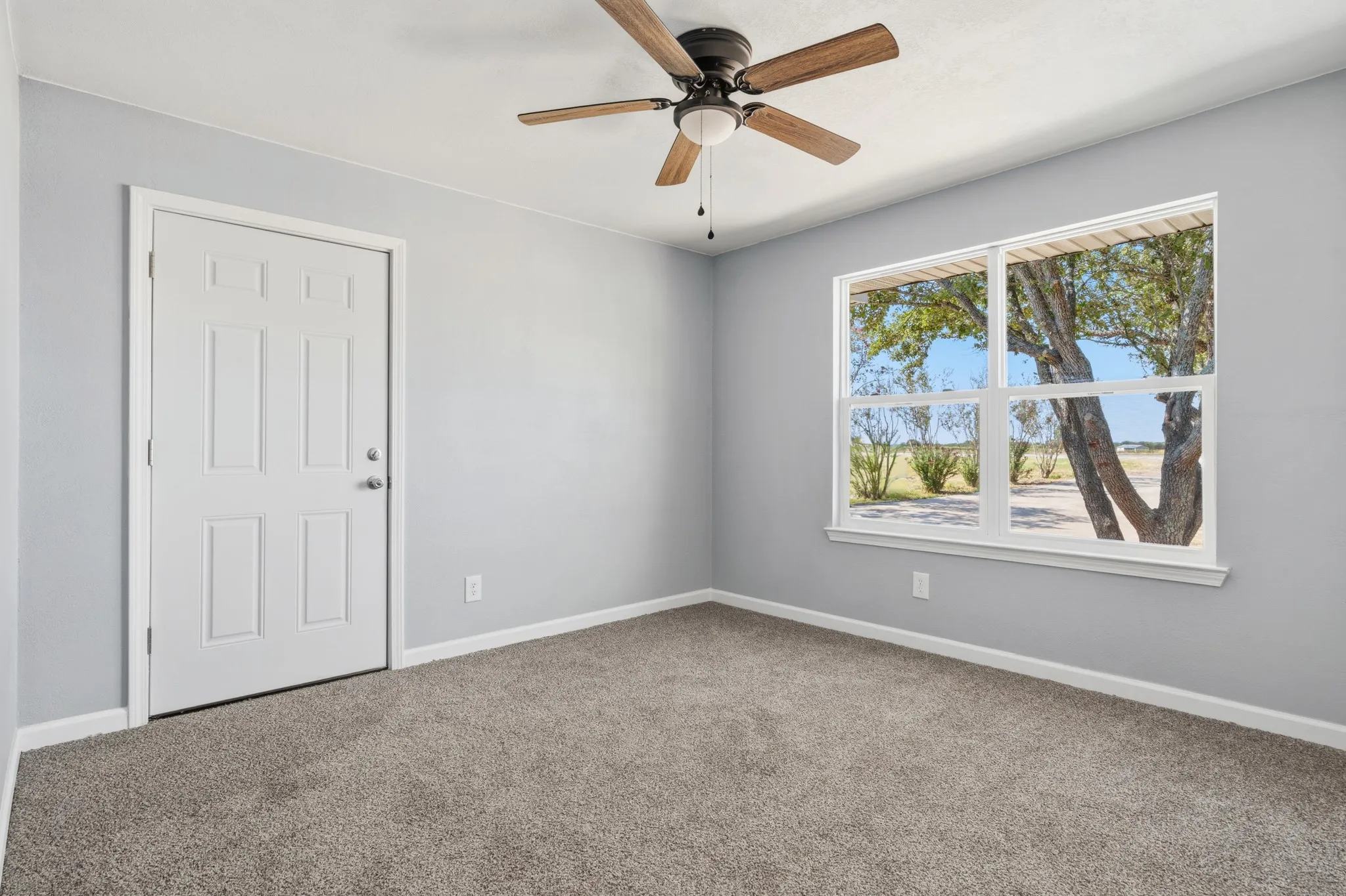 Neutral wall color, carpet flooring, ceiling fan with light fixture, paneled door, and a large window