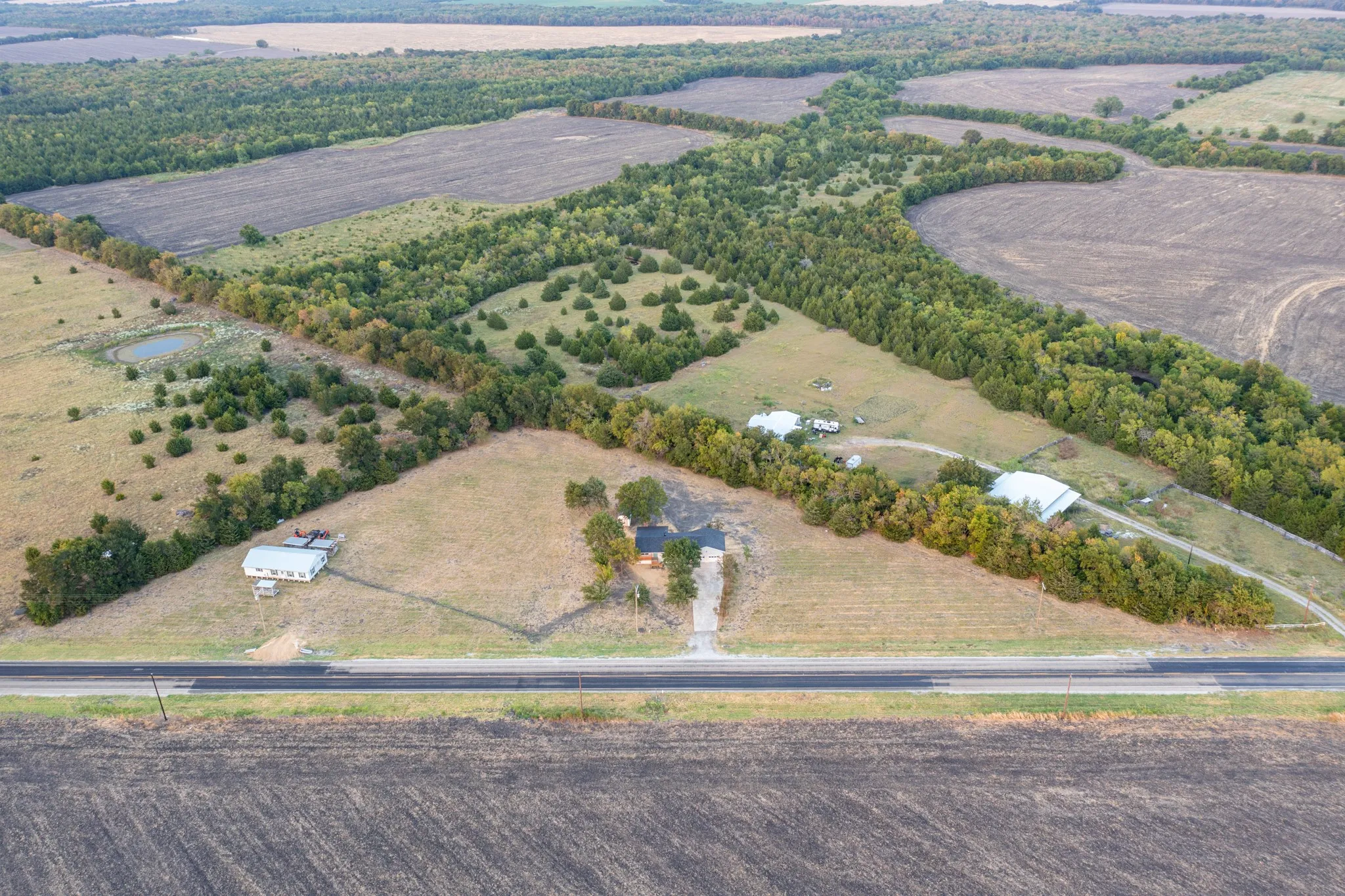 Expansive rural property featuring a main residence, additional structures, and a pond