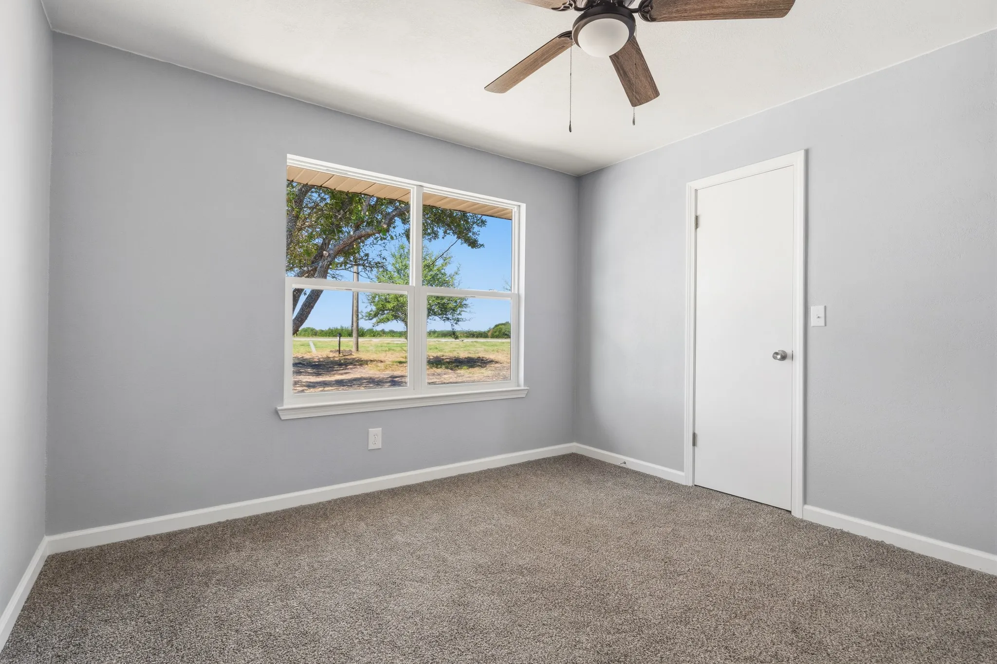 Carpeted room with a ceiling fan, a window, and a door