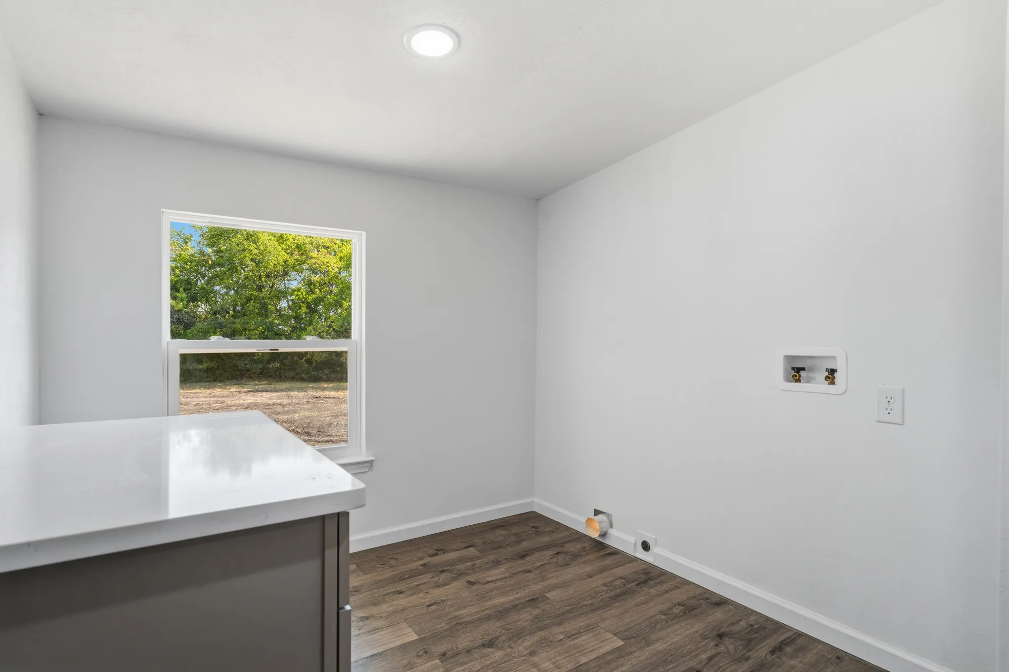 Recessed ceiling lighting, wood-finish flooring, white walls, built-in countertop, and a window