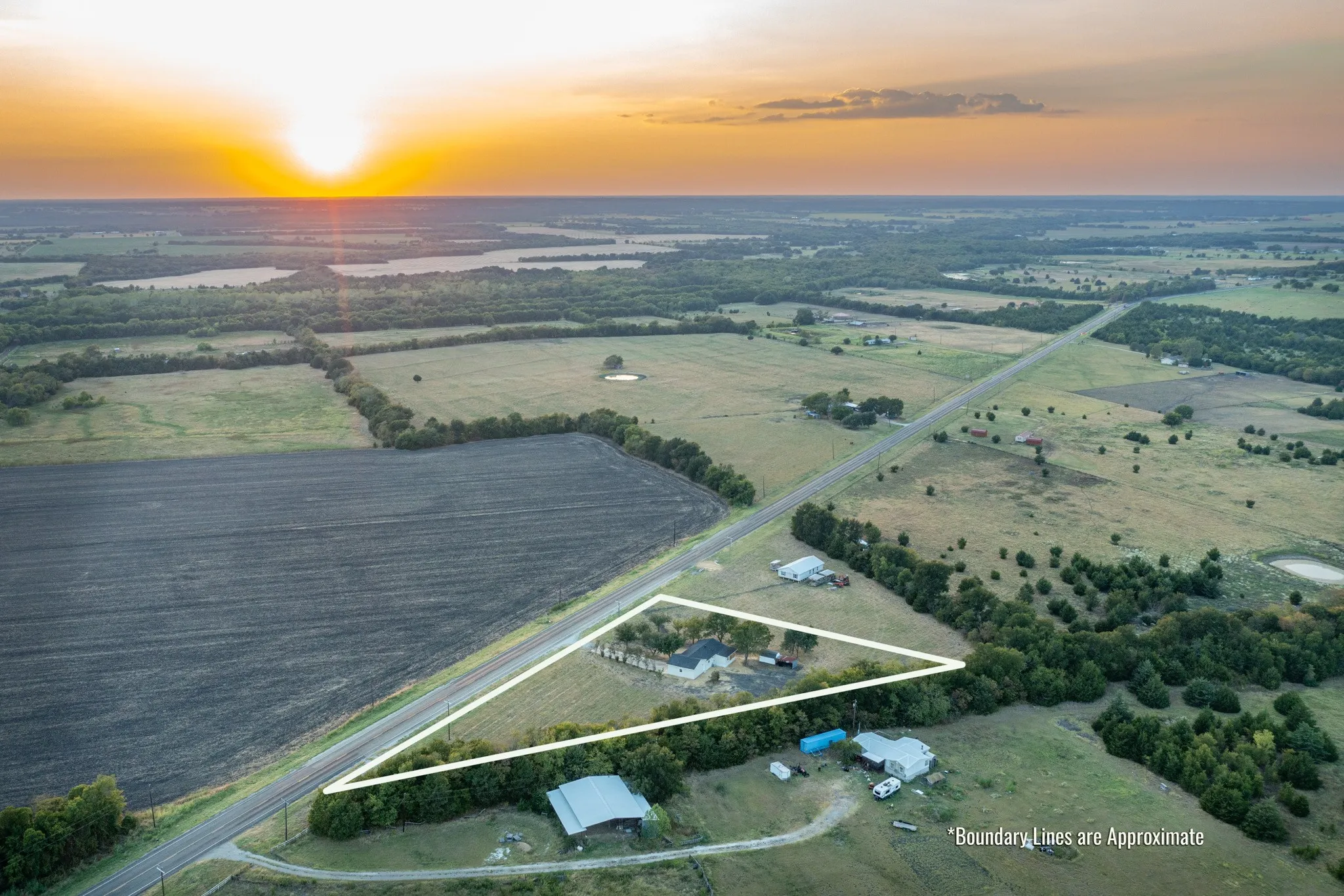 boundary lines are approximate. Expansive acreage featuring a single-story residence with outbuildings, dense tree lines, and a paved road frontage