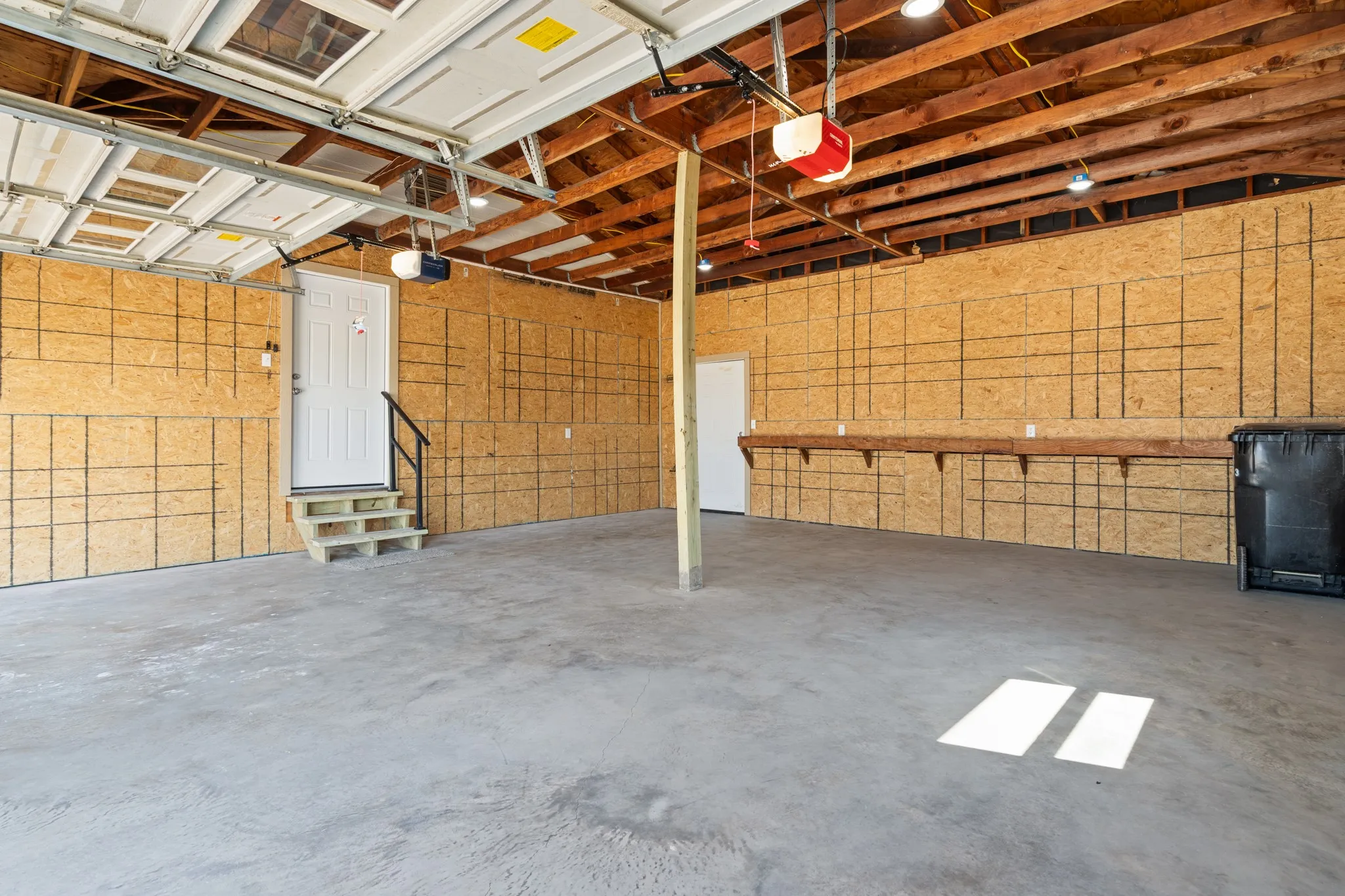 Exposed wood beam ceiling, concrete flooring, built-in shelving, two interior doors, and a garage door with translucent panels