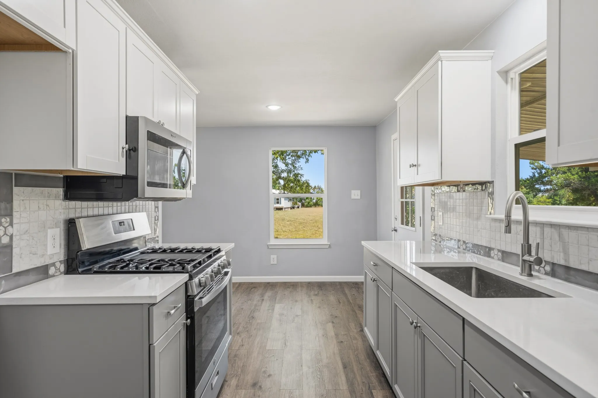 Galley kitchen featuring white upper cabinetry, gray lower cabinetry, stainless steel appliances, a tile backsplash, and light-toned countertops