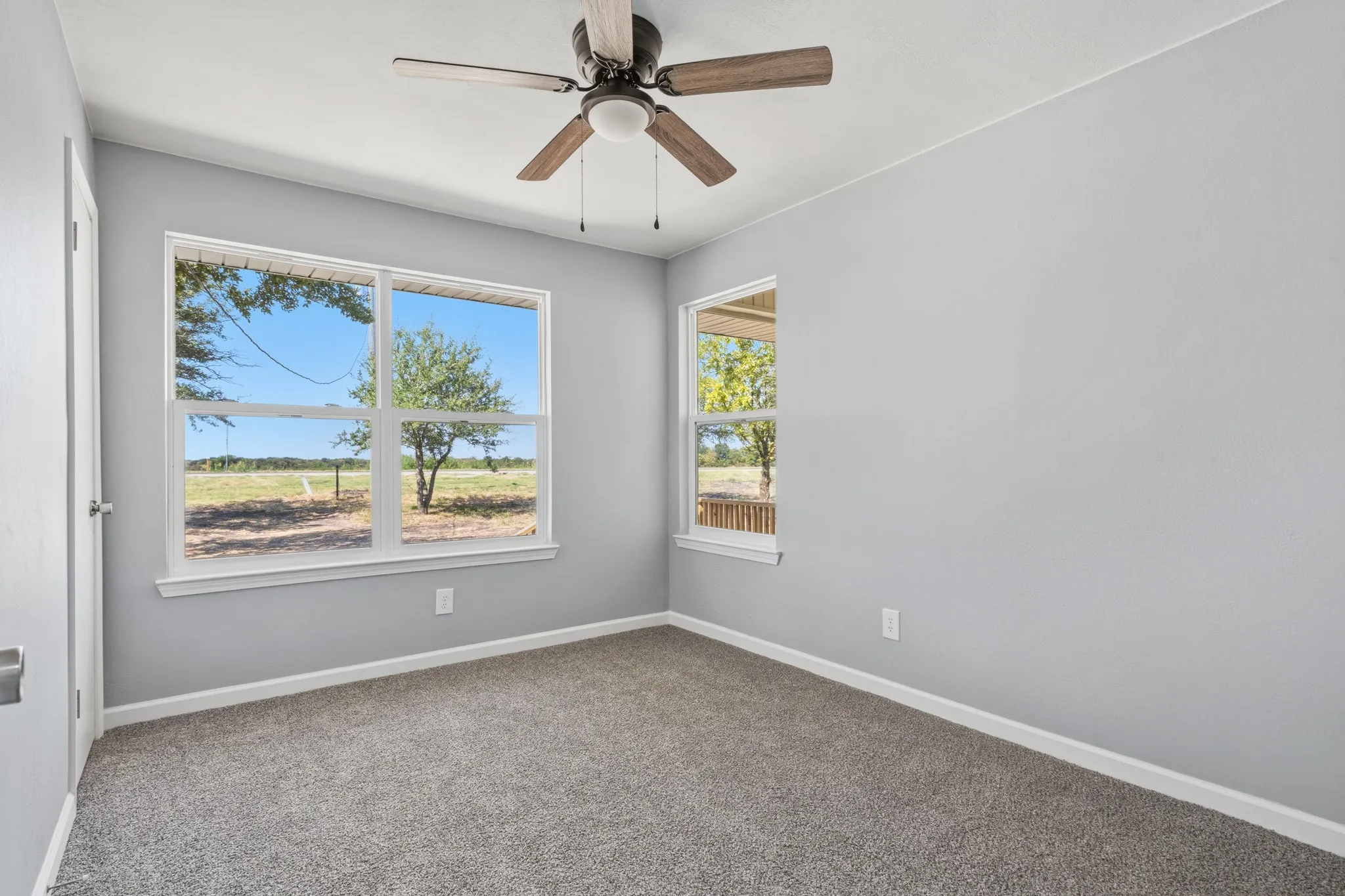 Carpeted room with light gray wall paint, two windows, and a ceiling fan with wood-finish blades