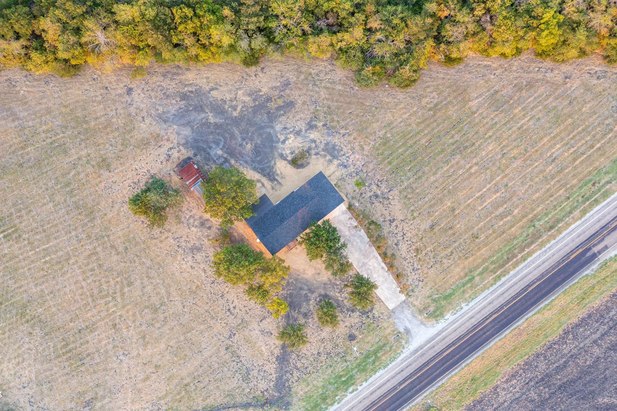 Expansive rural property featuring a single-story residence with a dark-shingle roof, mature trees, a long concrete driveway, and direct road access