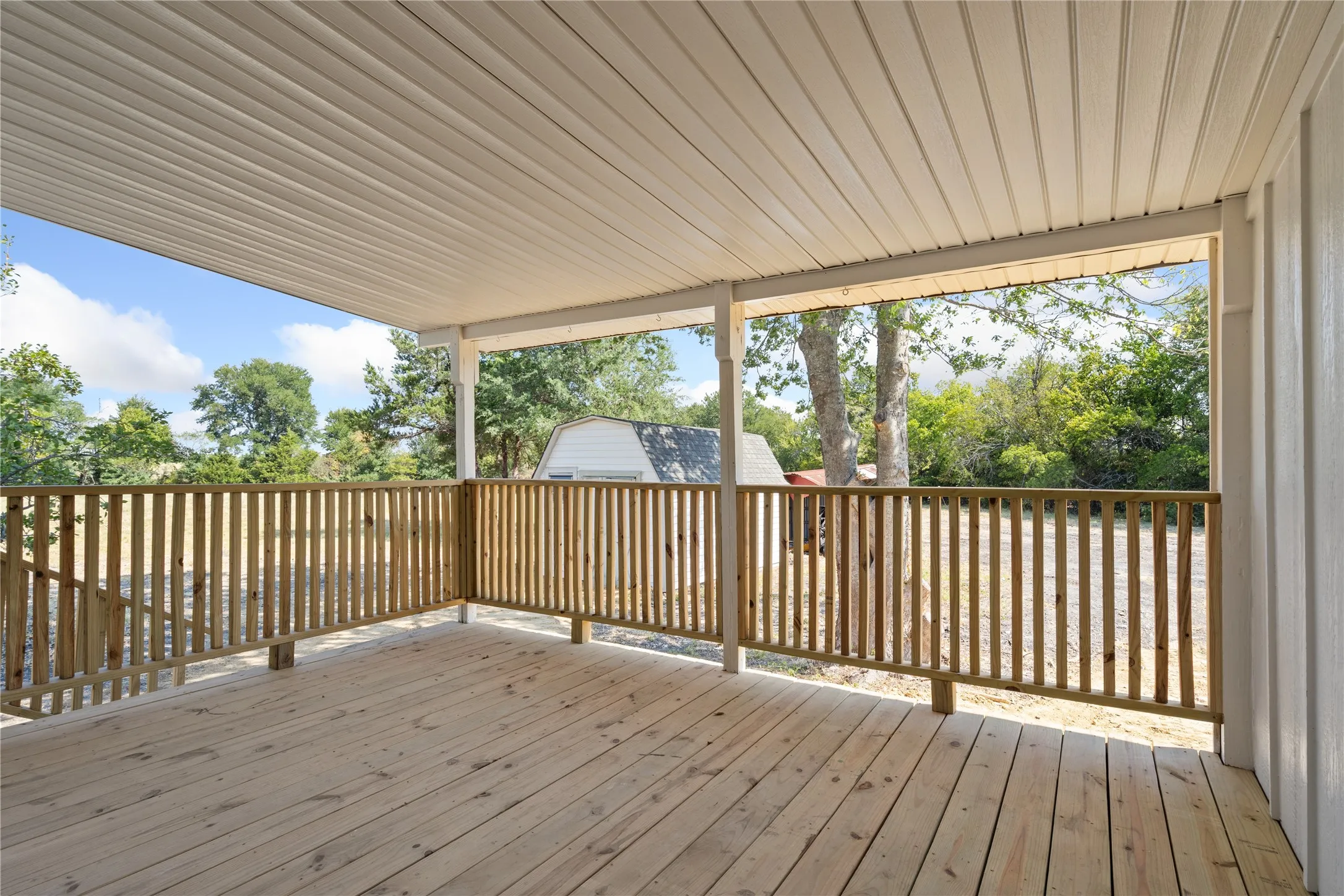 Covered outdoor deck featuring natural wood decking and railing, with a white paneled ceiling