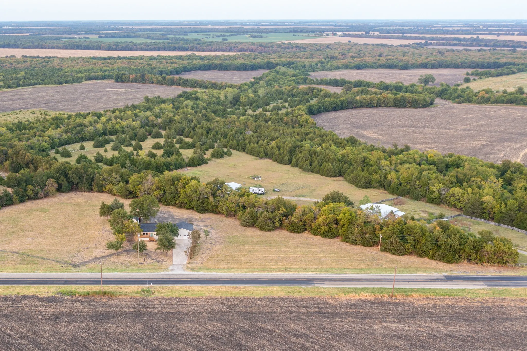 Expansive agricultural landscape featuring a single-story residence, mature trees, and an asphalt road