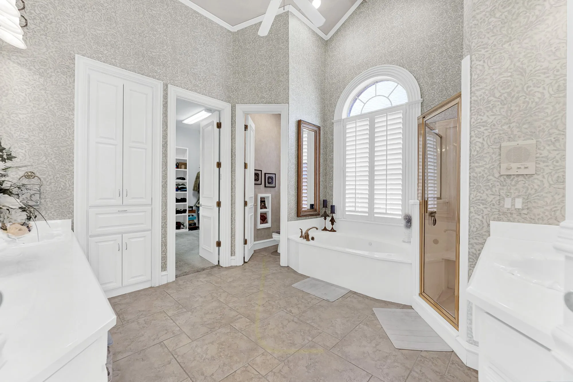An arched shuttered window casts soft daylight over the deep soaking tub tucked into a private corner. Indulge in a peaceful, spa-like bath after a busy week.