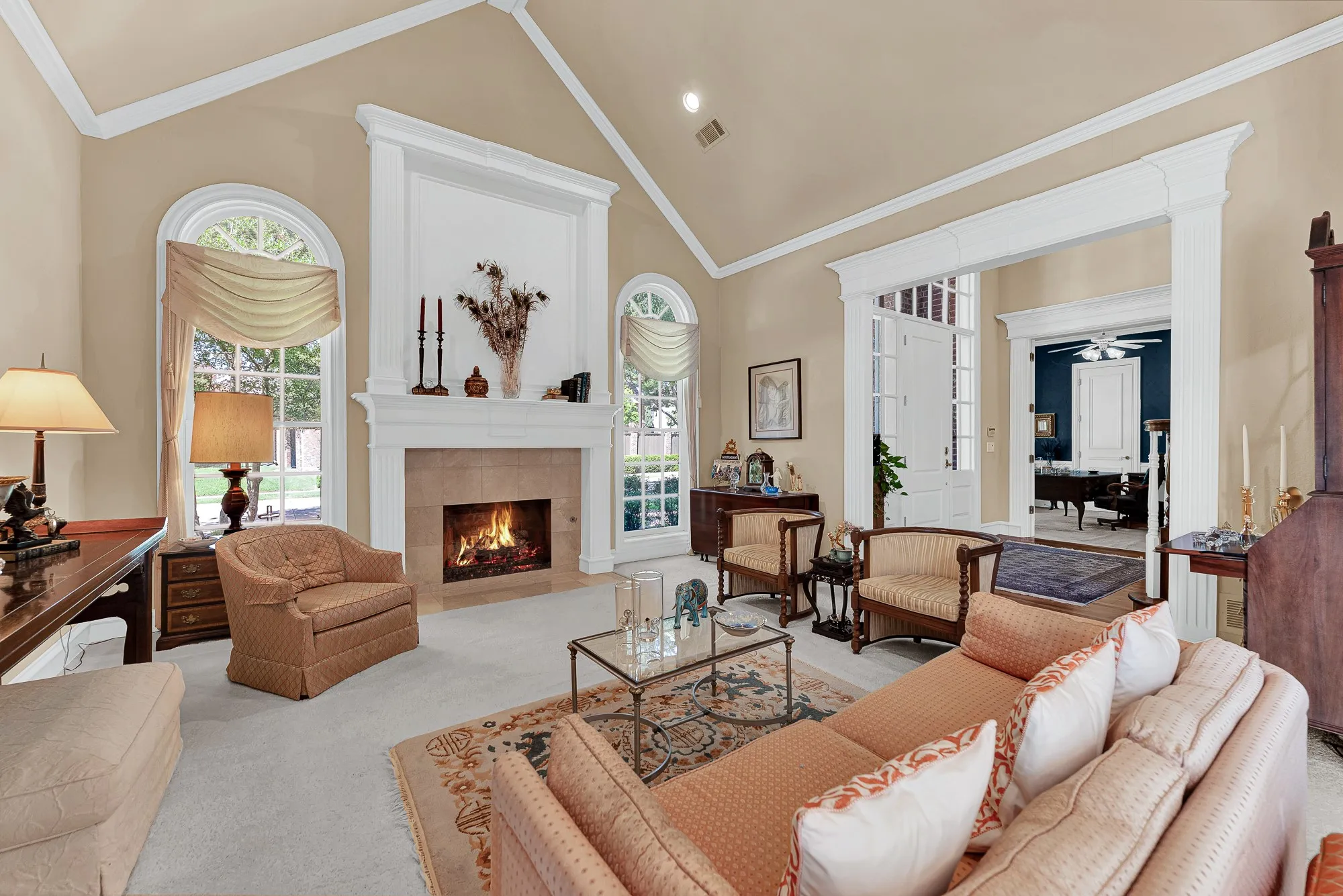 A grand fireplace mantle flanked by arched casement windows creates a striking central focal point beneath vaulted ceilings. Cozy up here on chilly winter evenings to unwind by the crackling hearth.