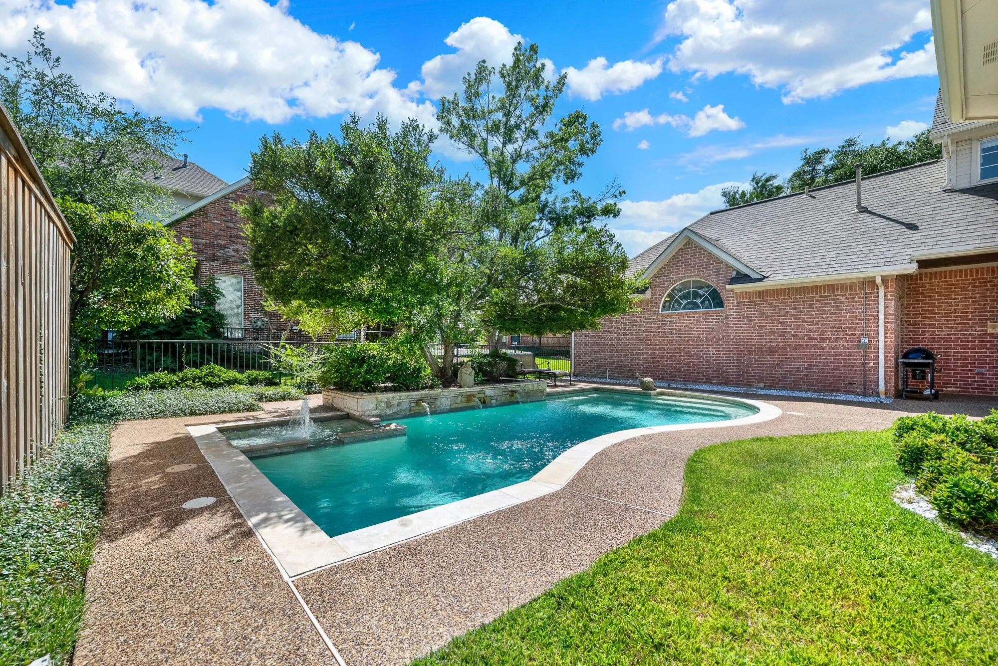 Lush lawn trim and stone garden coping outline the sparkling water feature against warm brick architecture. Host sunny weekend barbecues where guests can float lazily or splash in the clear water.
