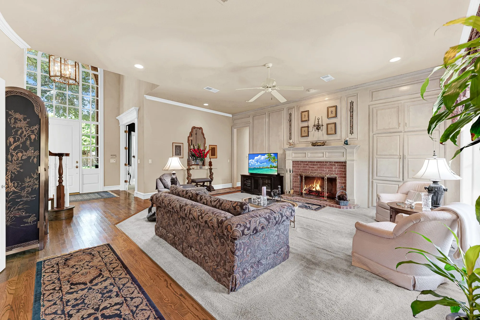 Detailed paneling surround and a classic brick fireplace anchor this soaring central living space. Picture hosting cozy movie nights with the family while a warm fire glows nearby