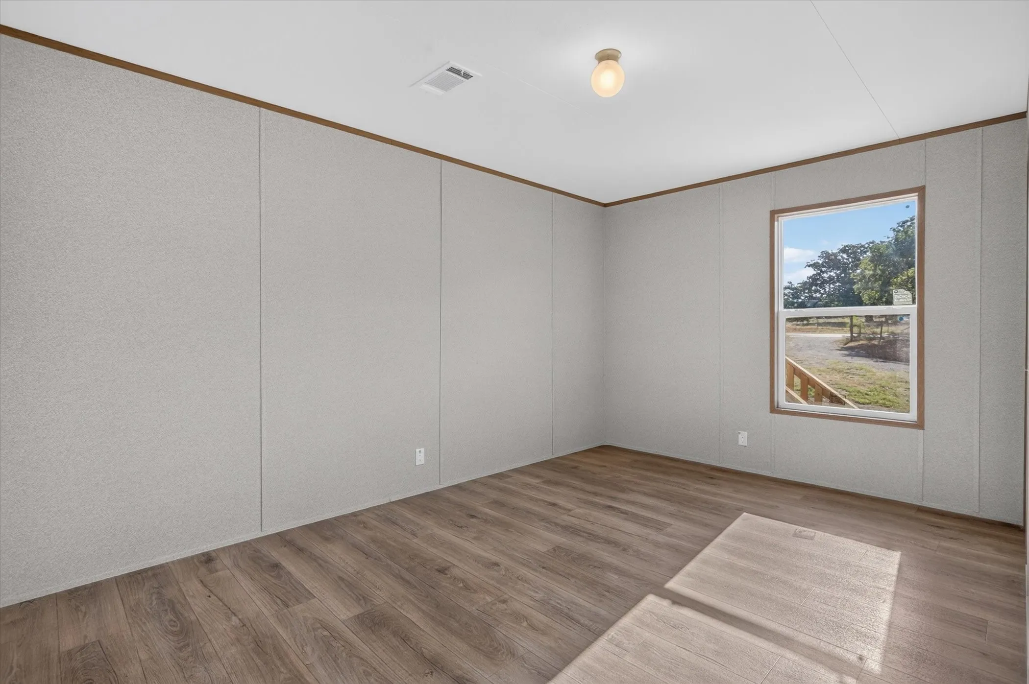Wood-finish flooring, light gray wall panels, window with exterior scenery, and ceiling-mounted light fixture