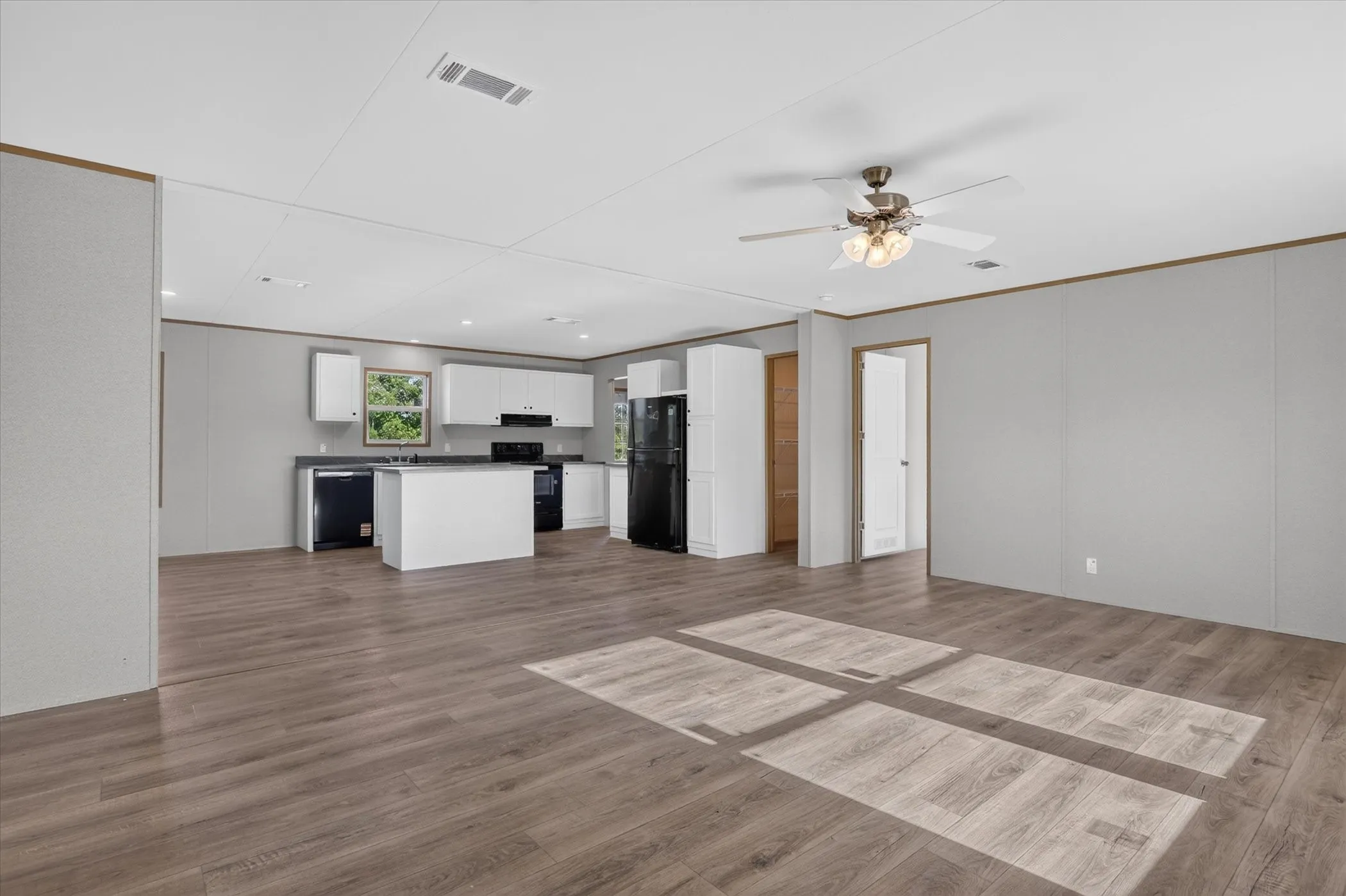 Open-concept living space featuring wood-finish flooring, a contemporary ceiling fan, and a kitchen with white cabinetry, black appliances, and an island