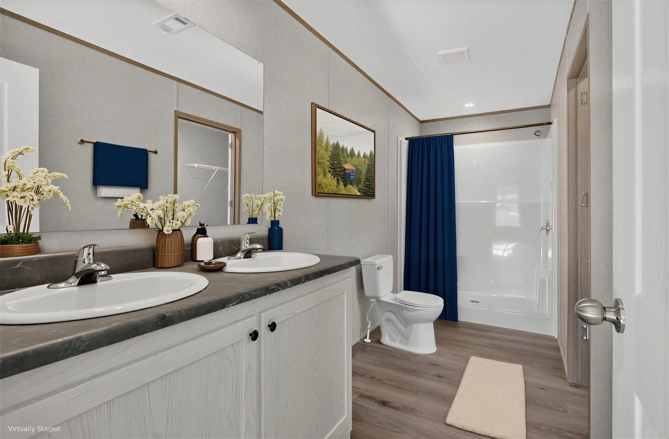 Double vanity with integrated sinks, gray-toned countertop, wood-finish flooring, full bath with shower, and white paneled walls