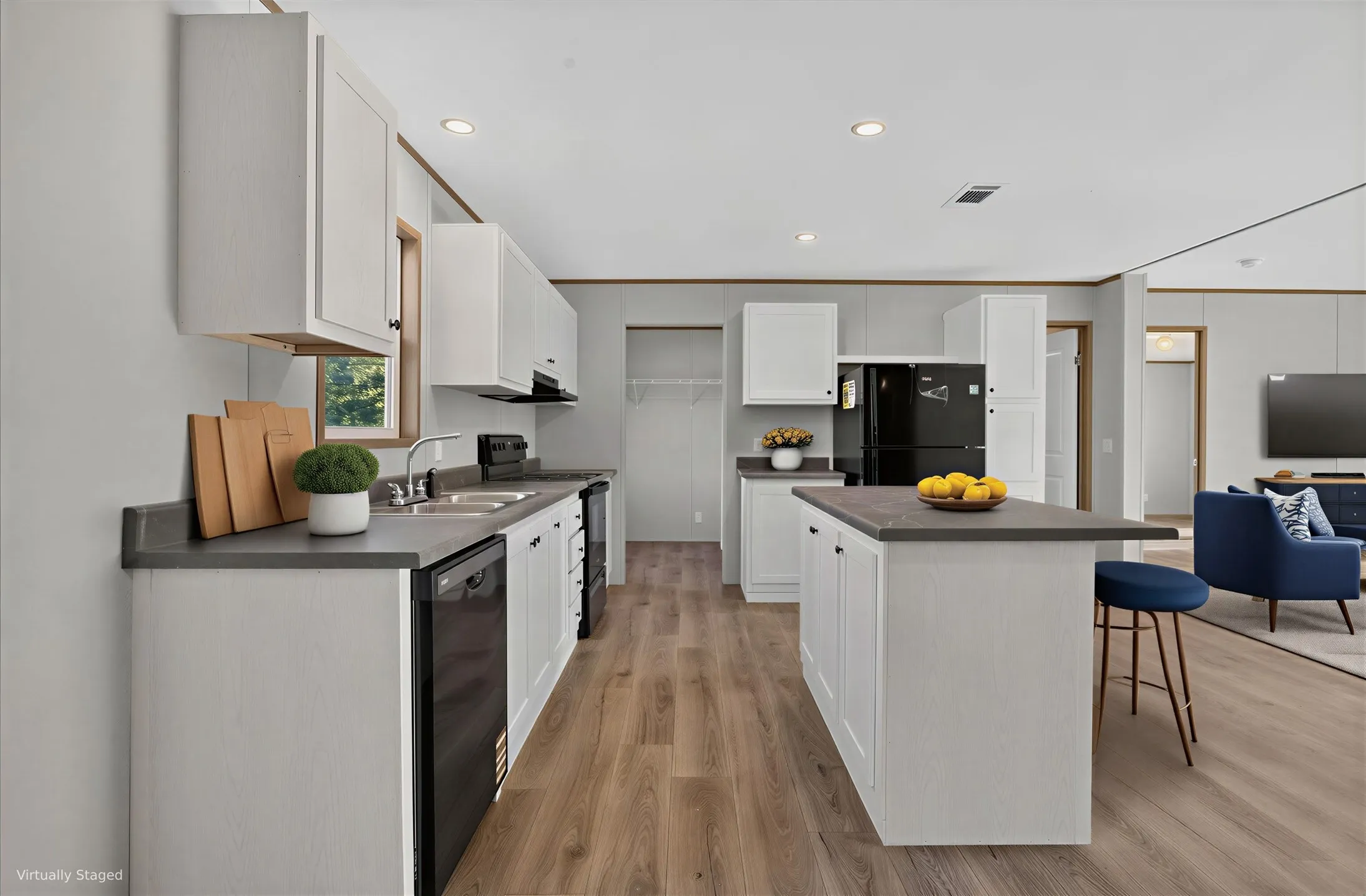 Kitchen featuring wood-finish flooring, white cabinetry, dark countertops, and a central island. Furniture is Virtually Staged