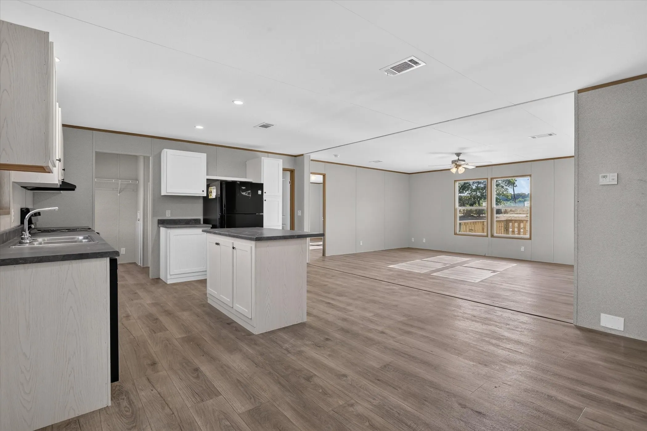 Open-concept living space with wood-finish flooring, white cabinetry, dark countertops, and a kitchen island