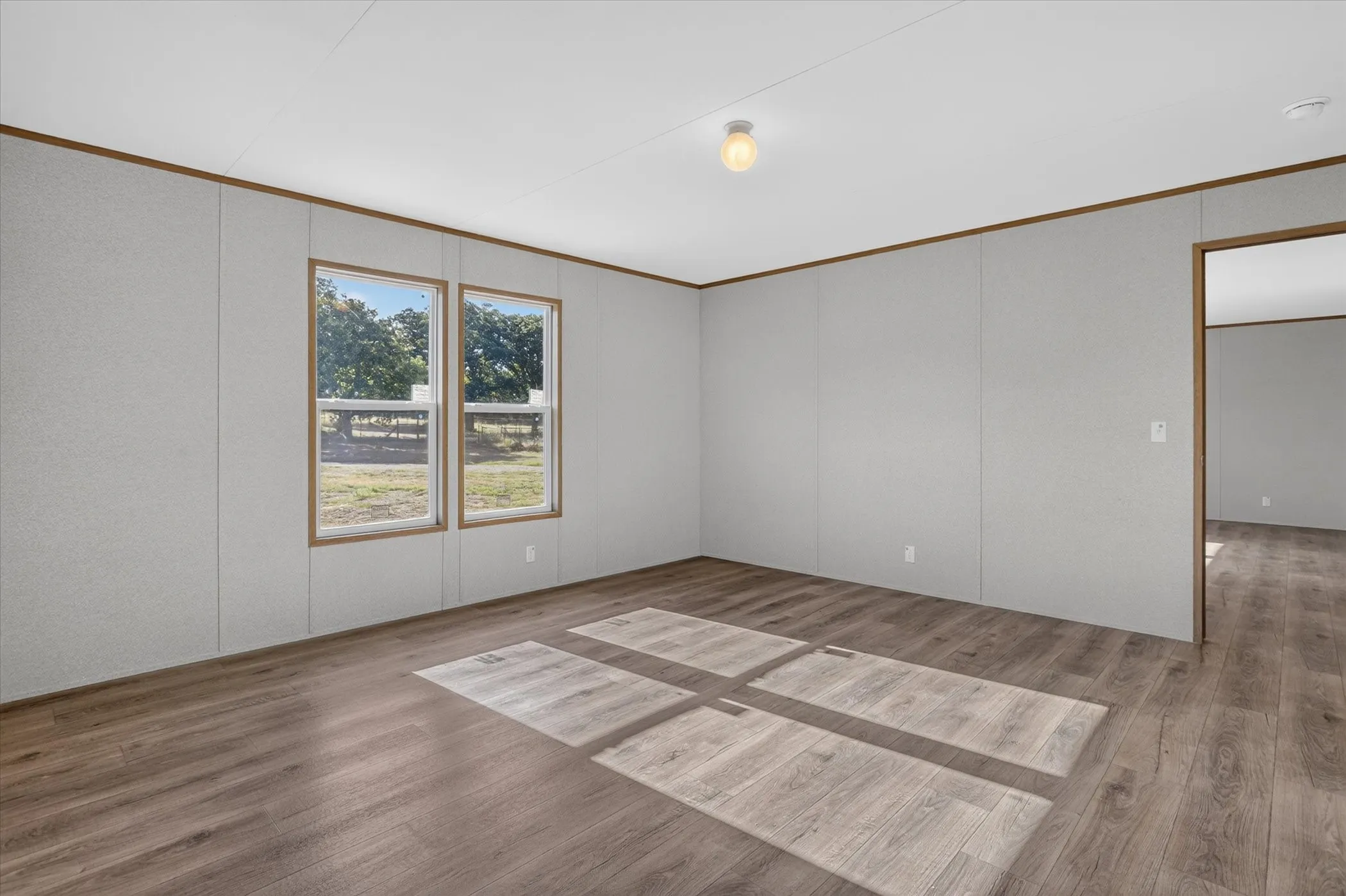 Wood-finish flooring, light grey paneled walls, and two large windows