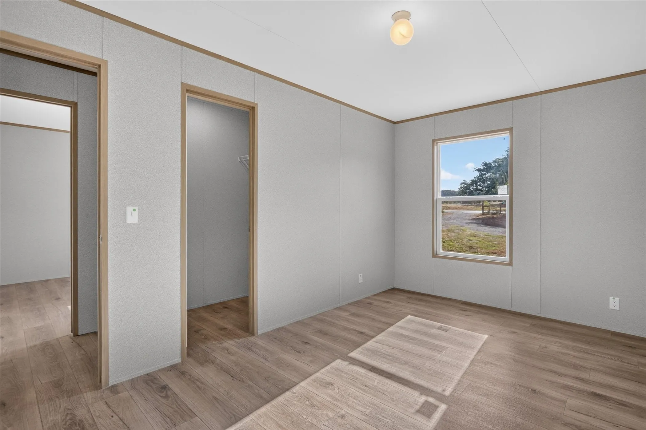 Wood-finish flooring throughout, light gray wall panels, and a single window offering natural illumination