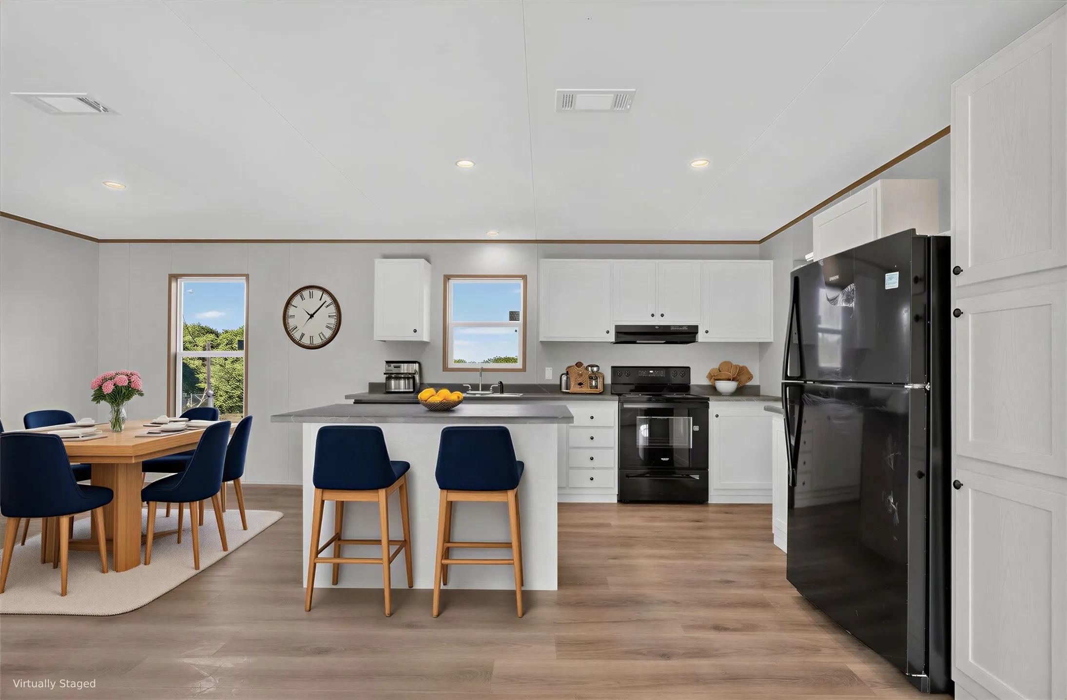 Open-concept kitchen and dining area featuring wood-finish flooring, white cabinetry, a kitchen island with seating, and a black appliance suite.Furniture is Virtually Staged