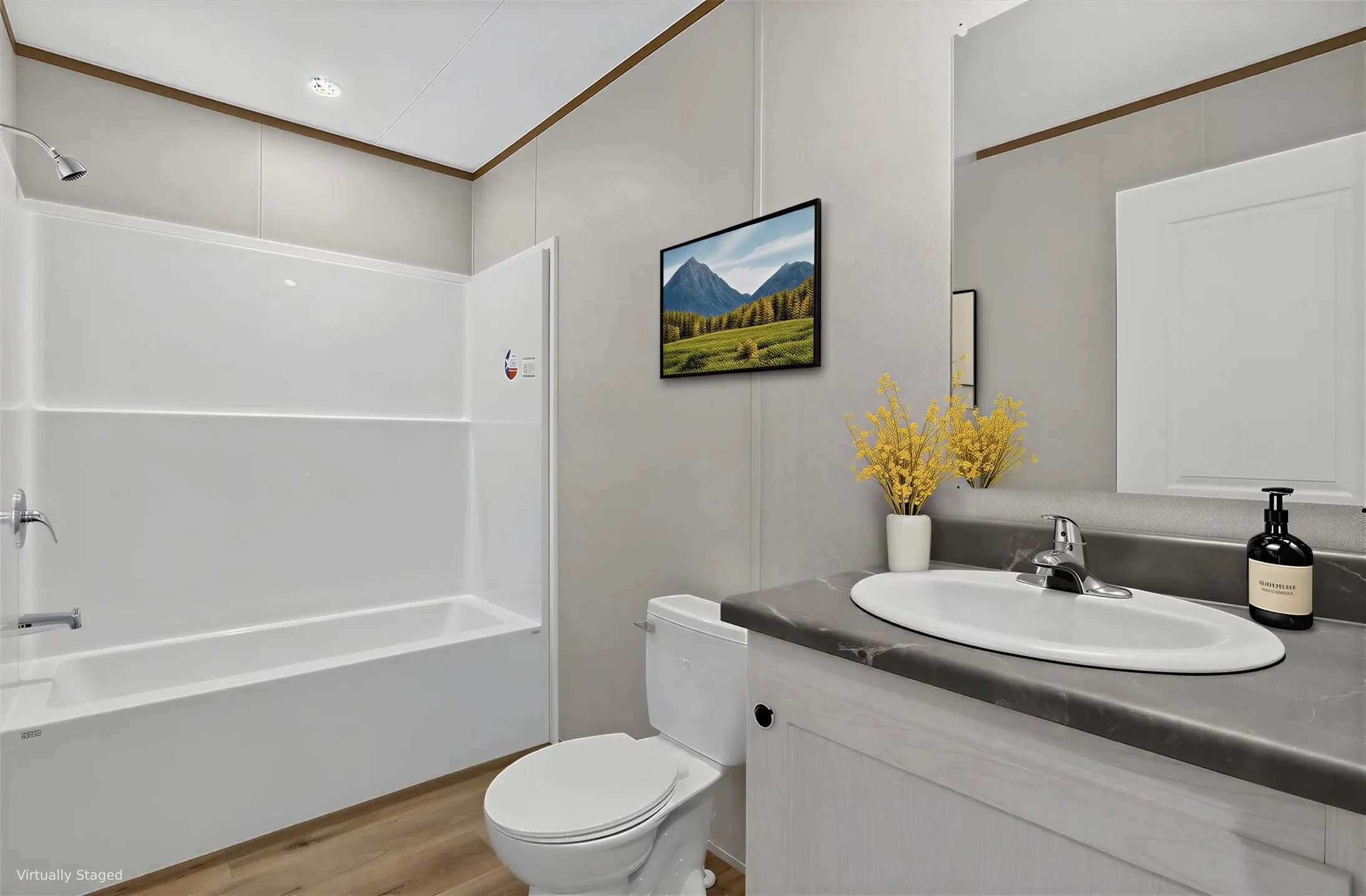 White bathtub with an integrated shower, wood-finish flooring, white vanity with a dark countertop, and a built-in mirror