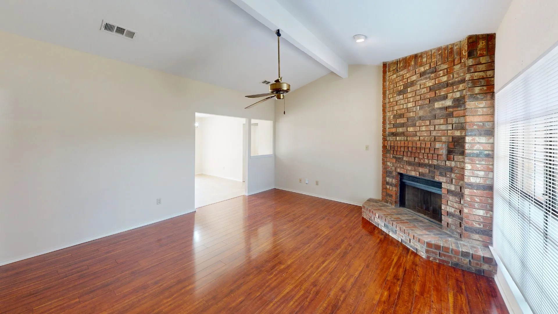 Vaulted ceiling with exposed beam, wood-finish flooring, brick-faced fireplace, and ceiling fan