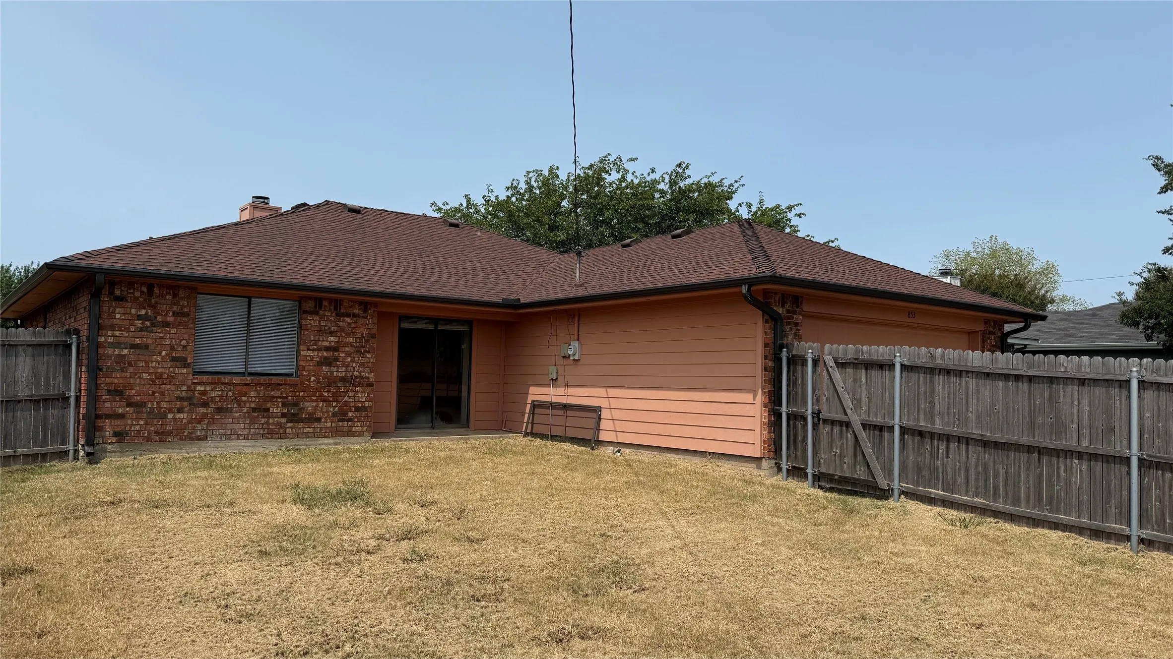 Rear exterior featuring brick and horizontal siding, composite shingle roofing, and a privacy fence