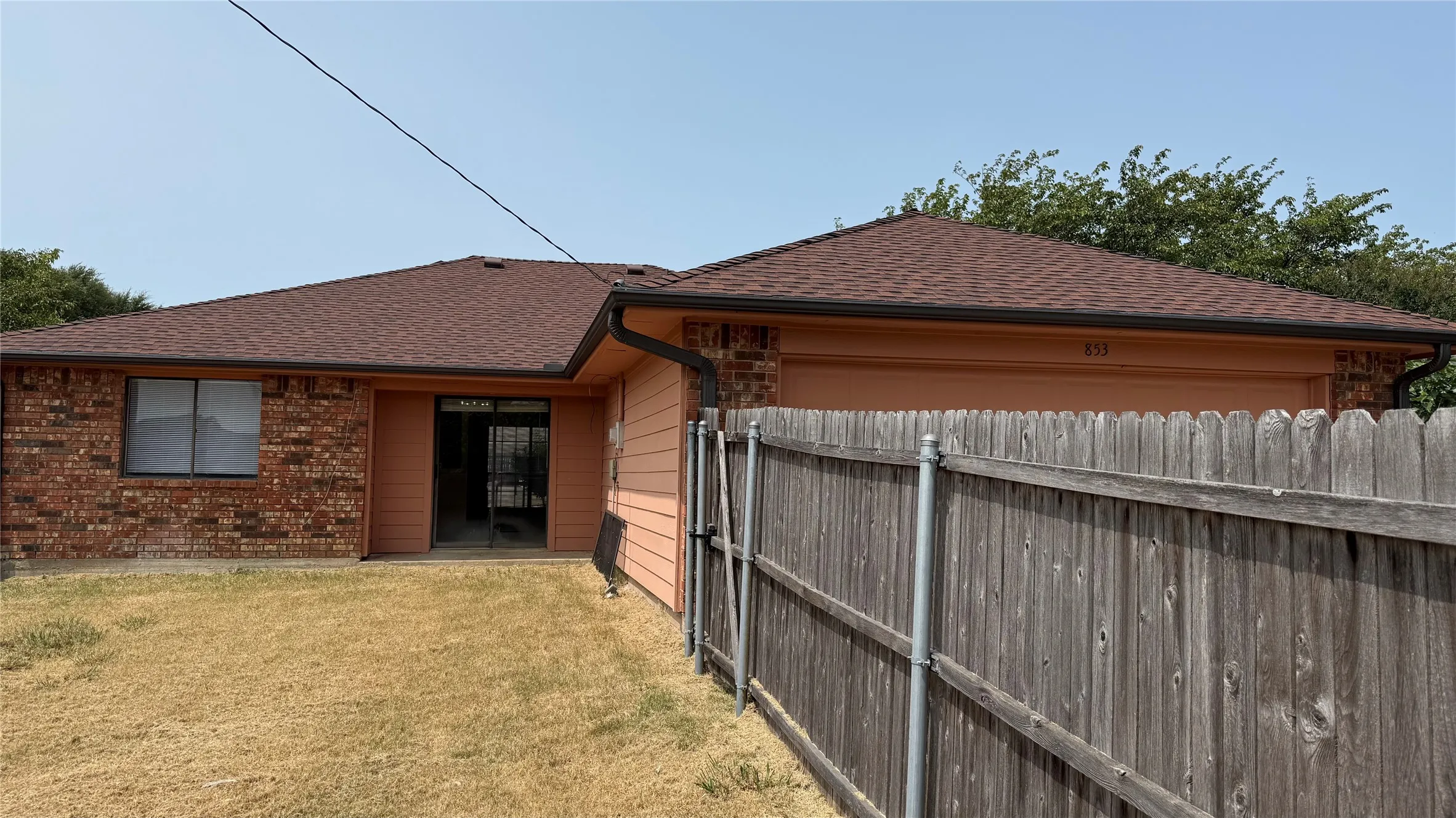 Brick exterior with a brown shingle roof, integrated garage, and a sliding glass door