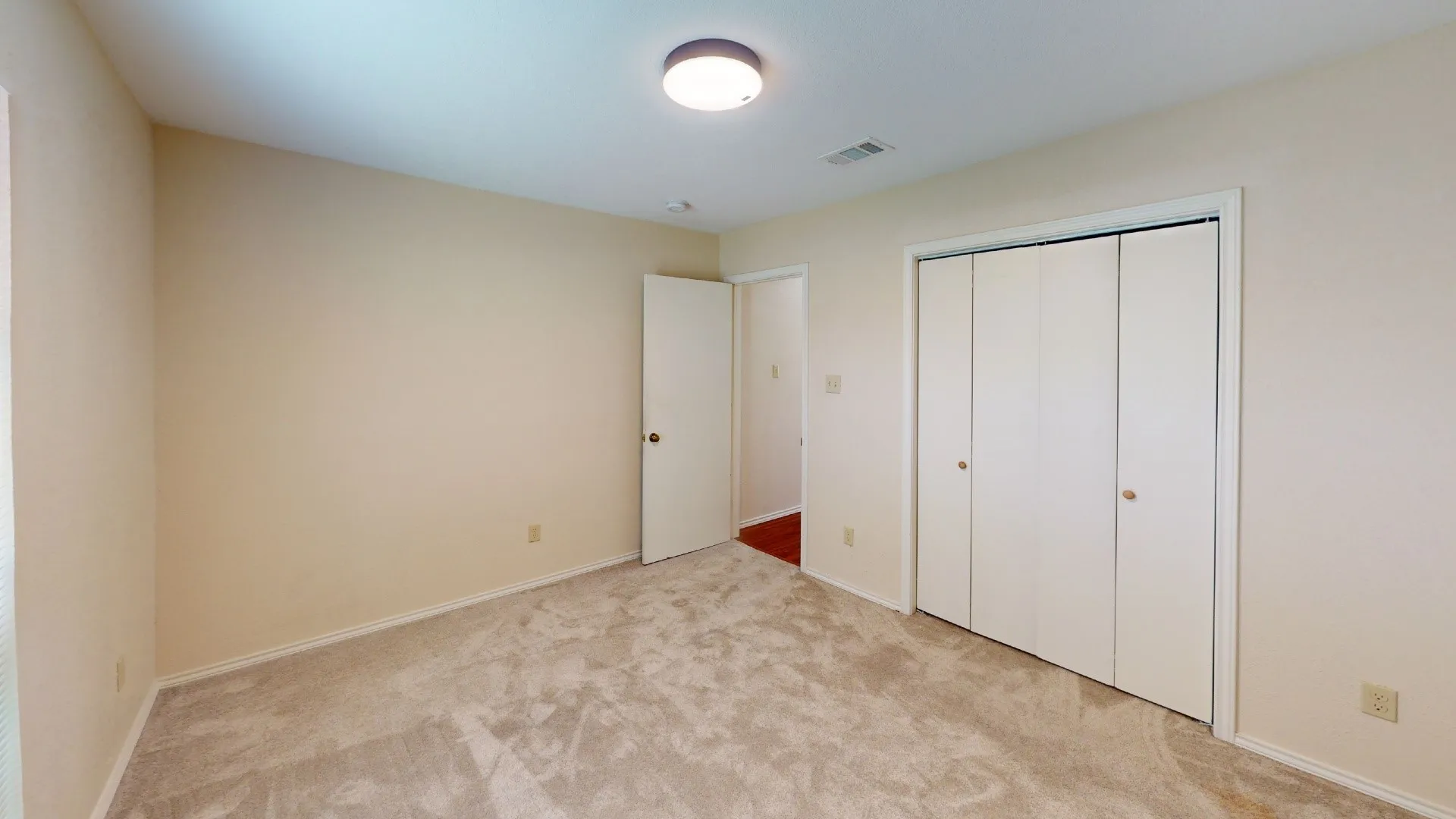 Neutral-toned walls, carpet flooring, flush mount lighting, and bi-fold closet doors