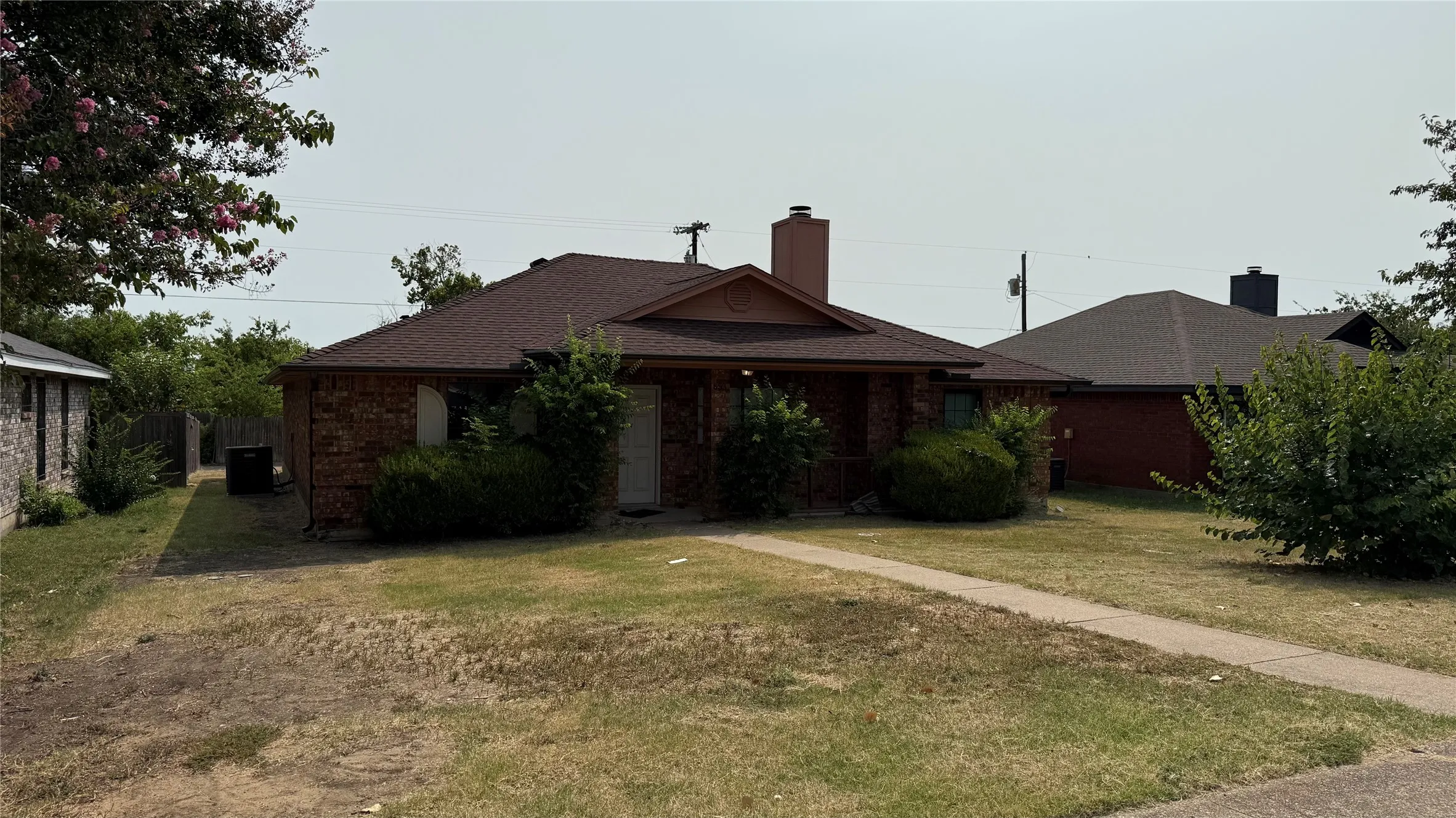 Brick exterior with a dark shingle roof and a concrete walkway