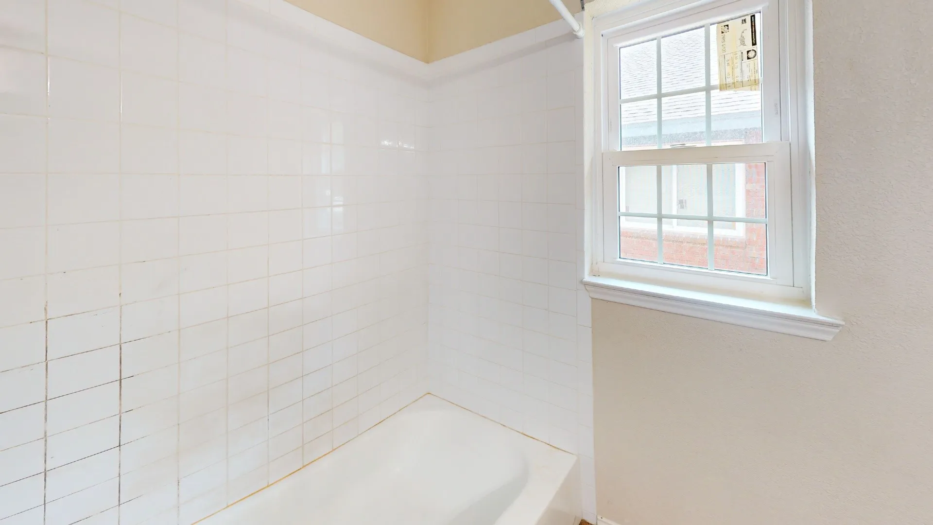 Bathtub with white subway tile surround and a window with white trim