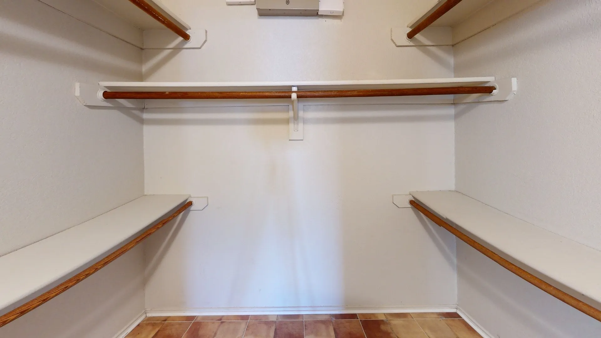 Closet space featuring multiple wood-finish hanging rods and white shelving