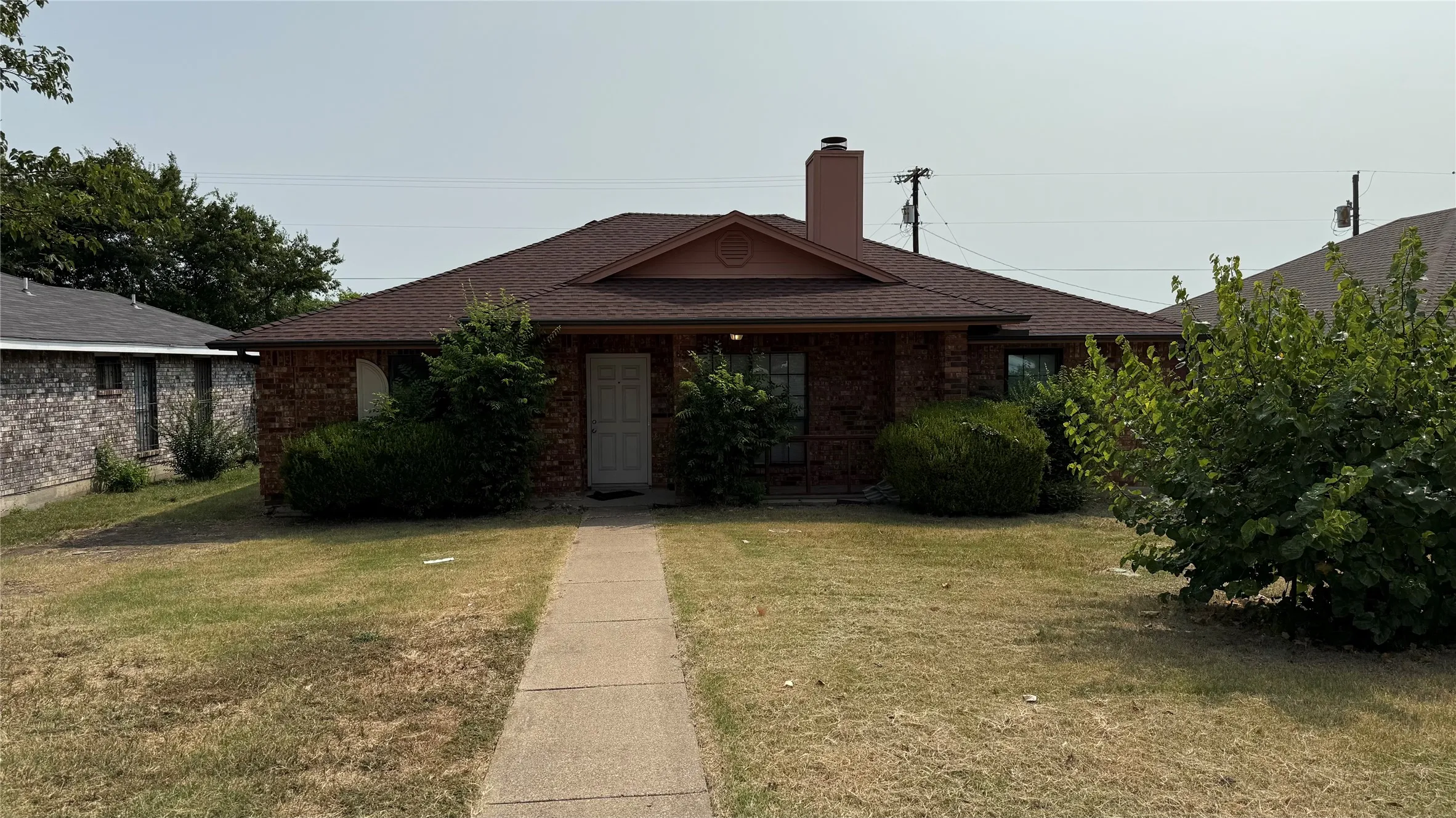 Brick exterior featuring a hip roof, prominent chimney, and a concrete pathway leading to the front entry