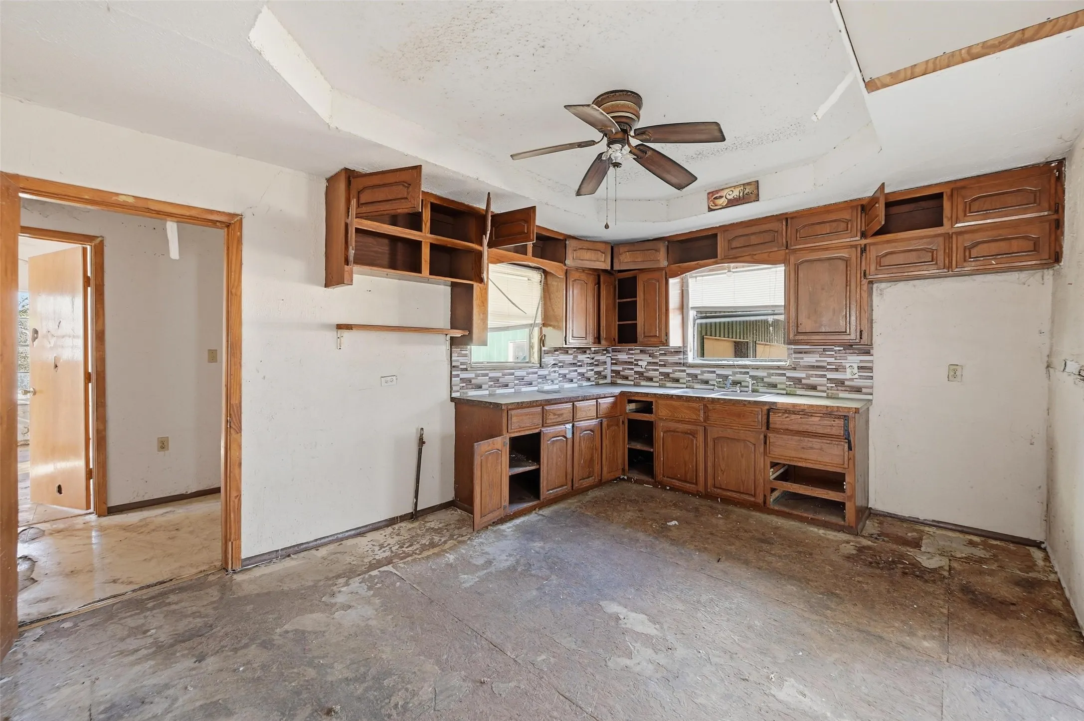 Kitchen with a raised ceiling, brown cabinets, ceiling fan, light countertops, and backsplash