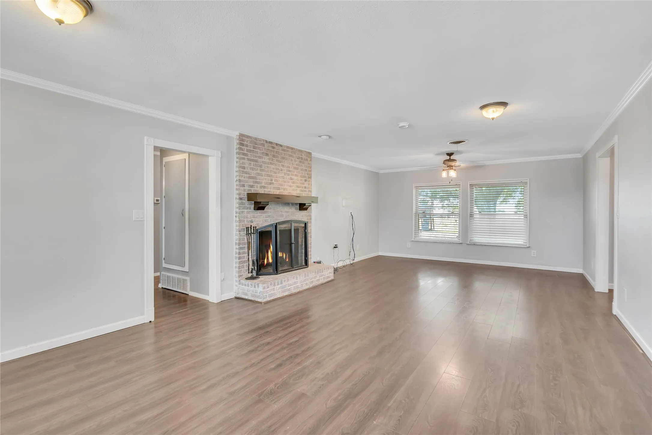 Spacious interior featuring wood-finish flooring, a brick fireplace with a wood mantle, multiple windows, and ceiling fan