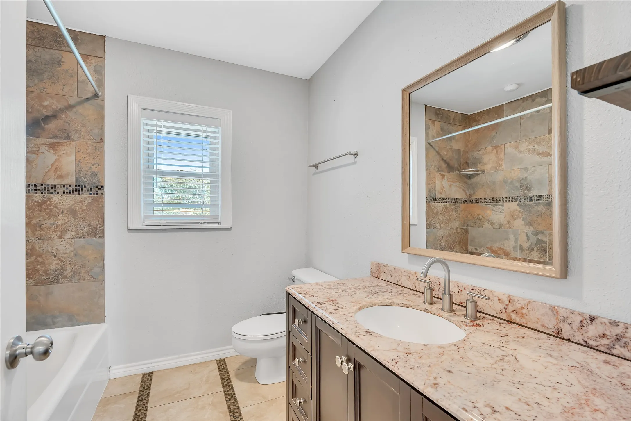 Bathroom featuring a brown wood-finish vanity with a light-toned countertop, an undermount sink, and a framed mirror