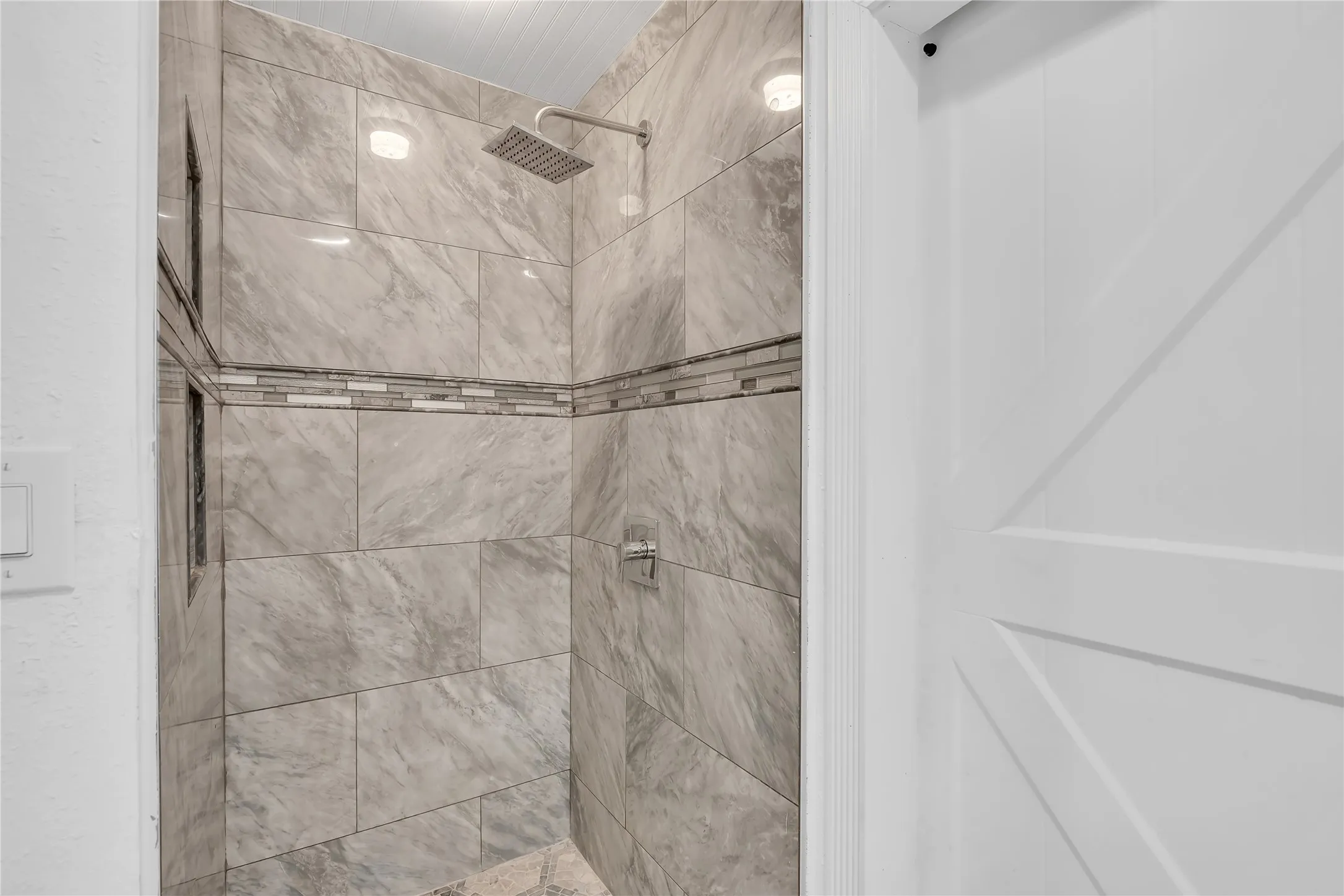 Tiled shower with a decorative mosaic accent band, rain shower head, and recessed lighting
