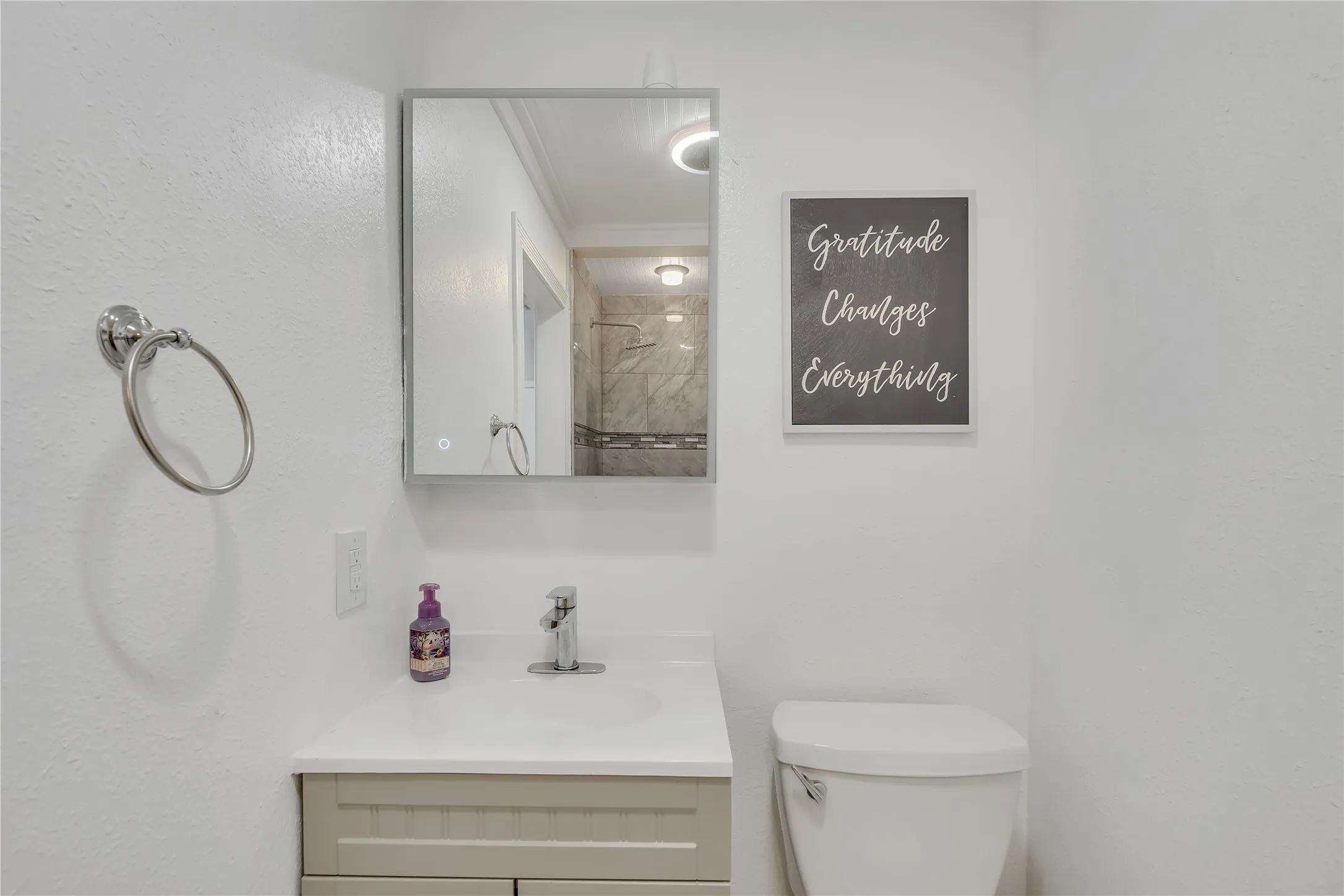Vanity with integrated sink, chrome faucet, wall-mounted mirror, and toilet