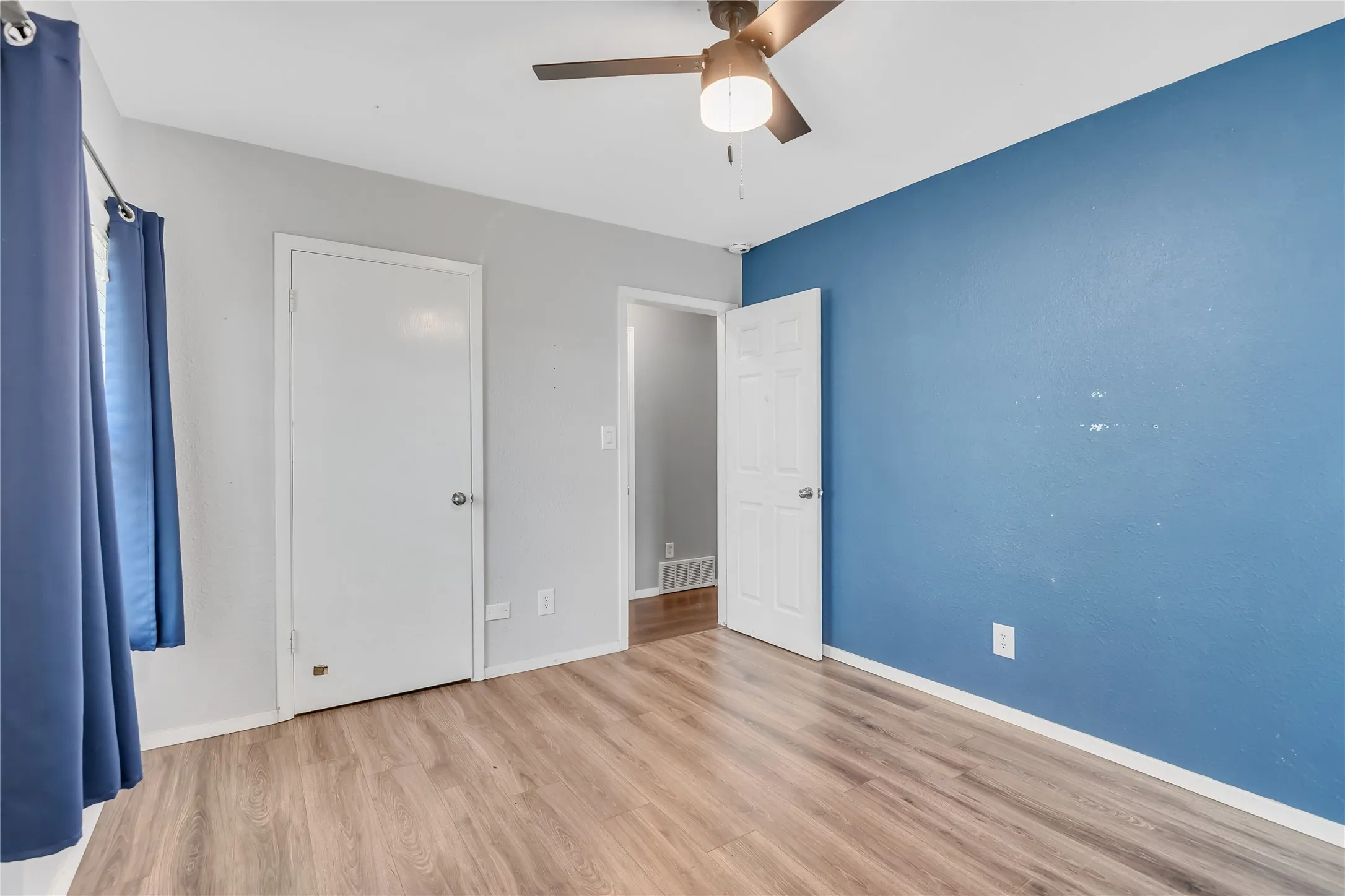 Wood-finish flooring, ceiling fan with integrated lighting, and multiple white panel doors
