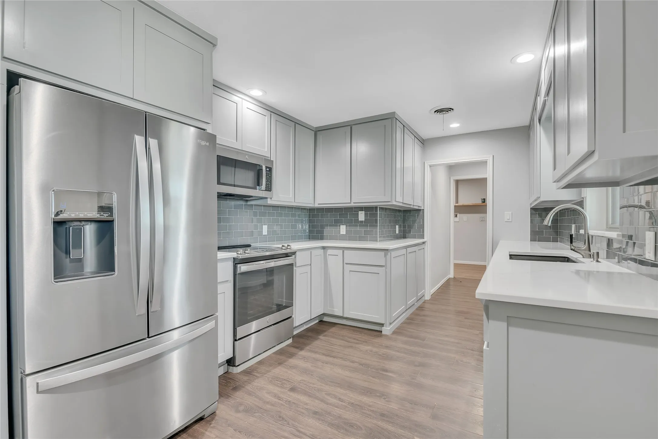Kitchen featuring stainless steel appliances, light gray cabinetry, white countertops, a tiled backsplash, and wood-finish flooring