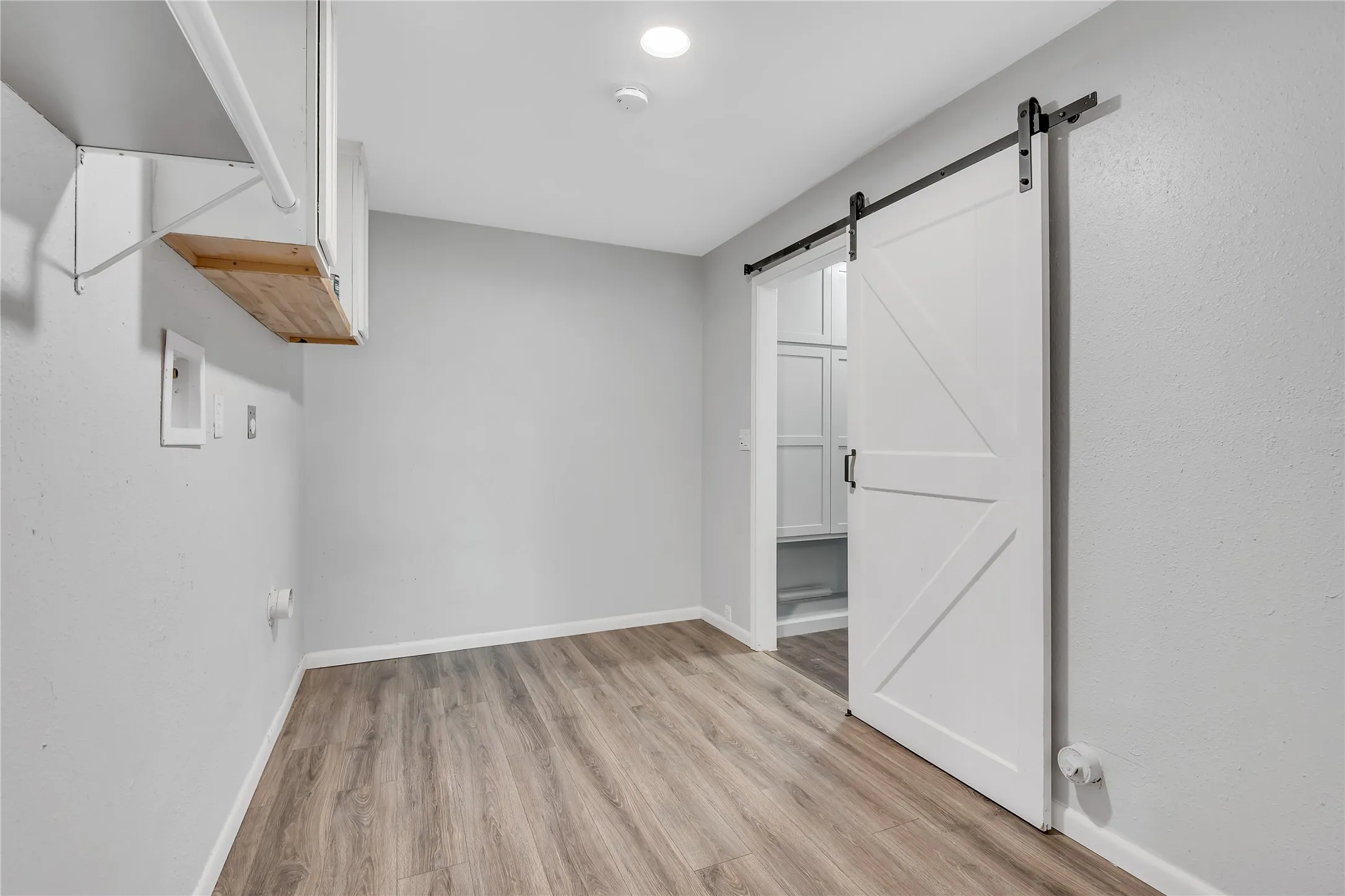 Wood-finish flooring, white barn door with black hardware, recessed ceiling lighting, and built-in shelving