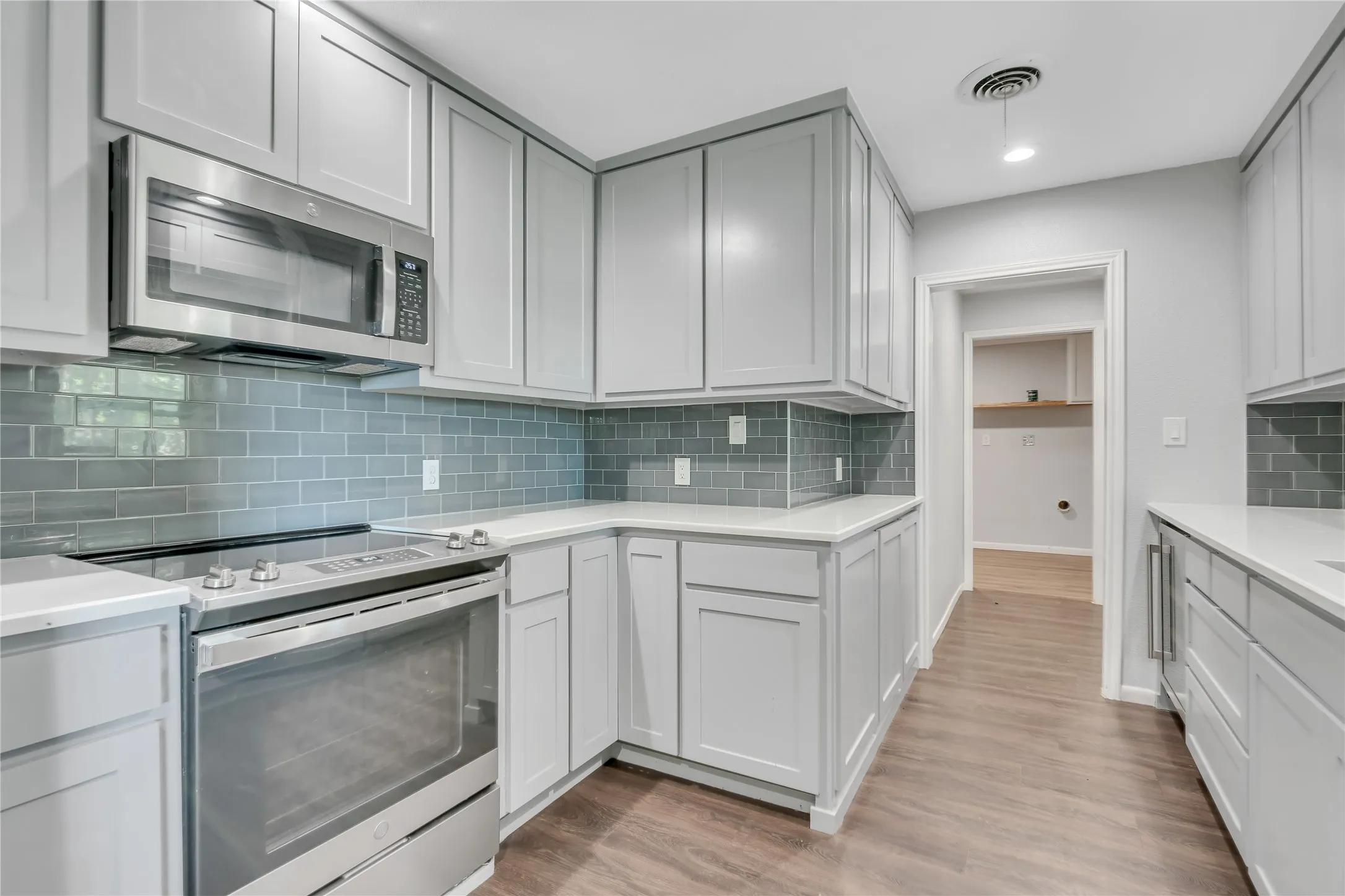 Kitchen featuring light gray cabinetry, white countertops, a subway tile backsplash, stainless steel appliances, and wood-finish flooring