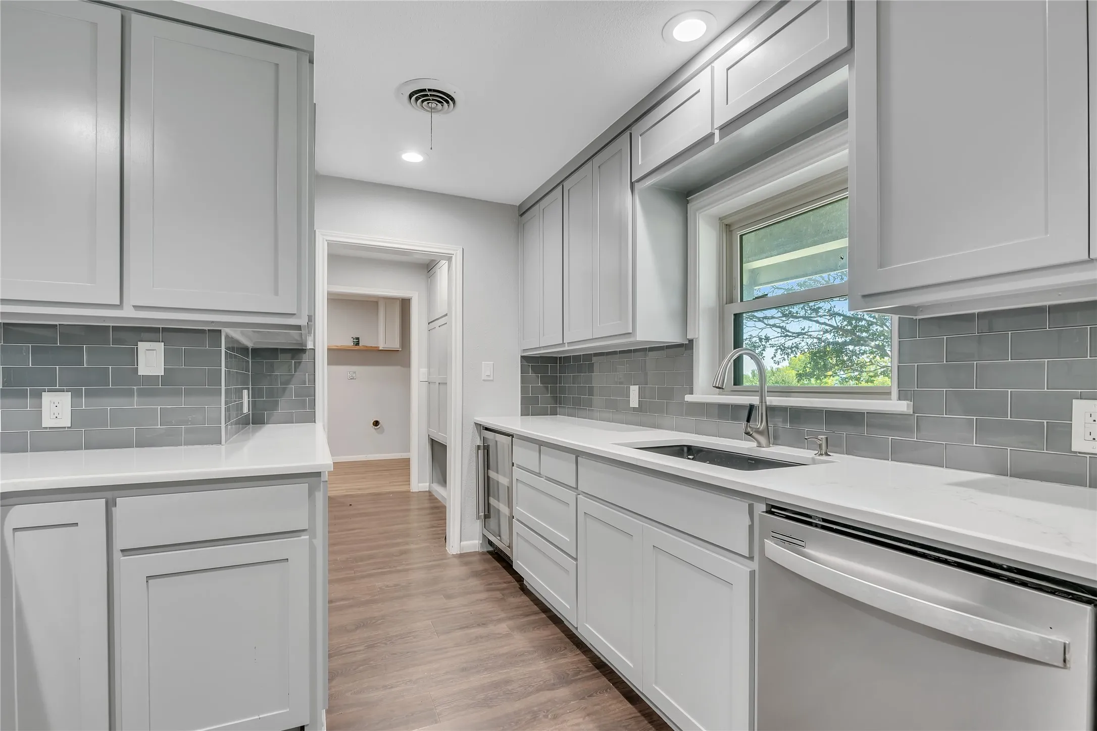 Contemporary kitchen featuring light gray shaker-style cabinetry, white countertops, and a gray subway tile backsplash