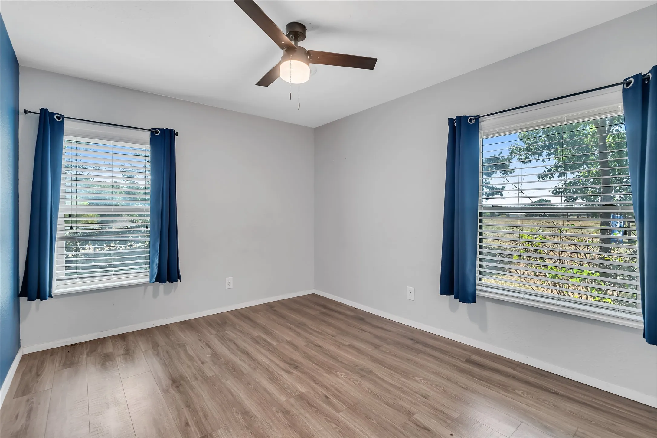 Wood-finish flooring with a ceiling fan and two windows