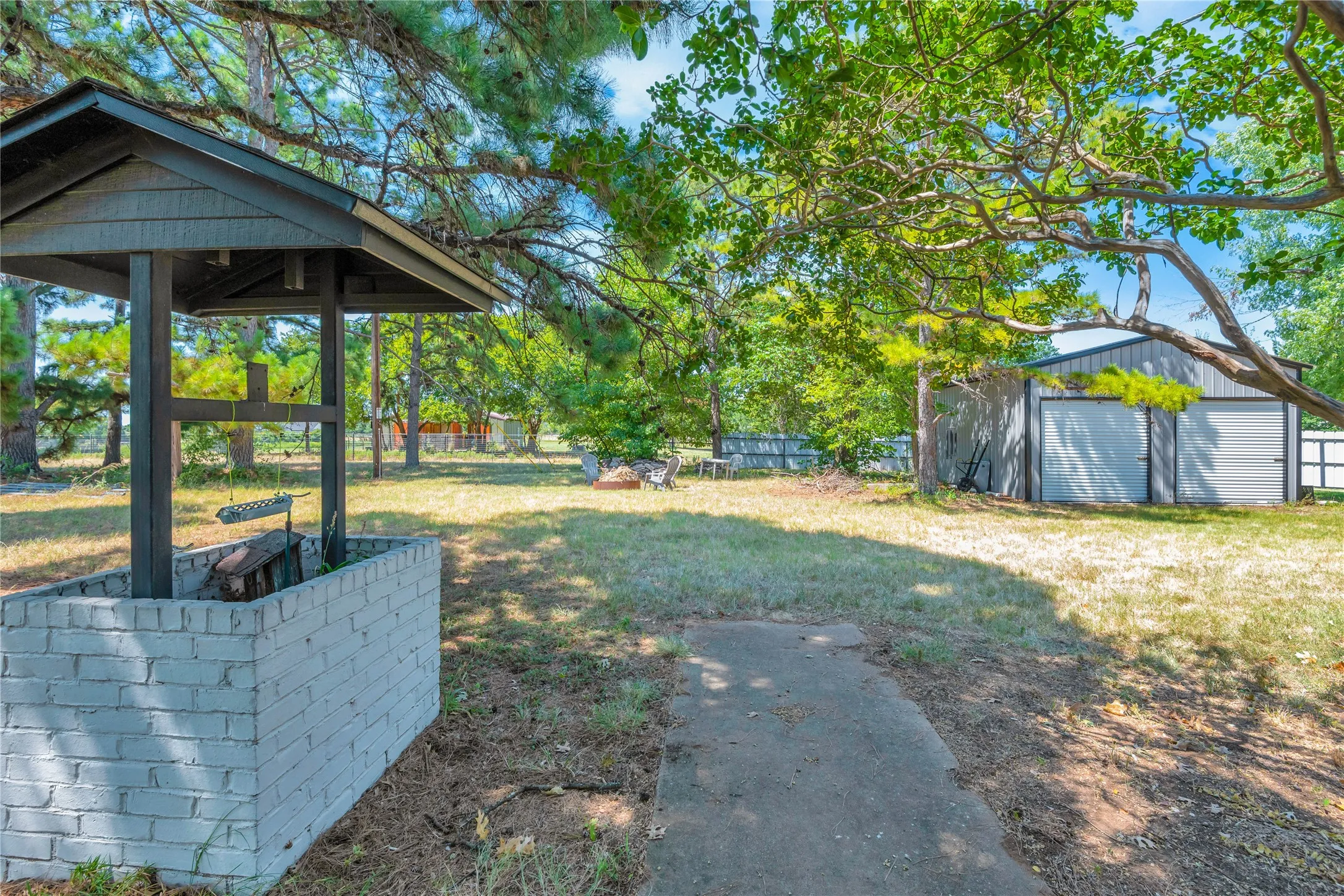 Expansive outdoor space featuring a well structure with a brick base, mature trees, and a two-bay detached garage