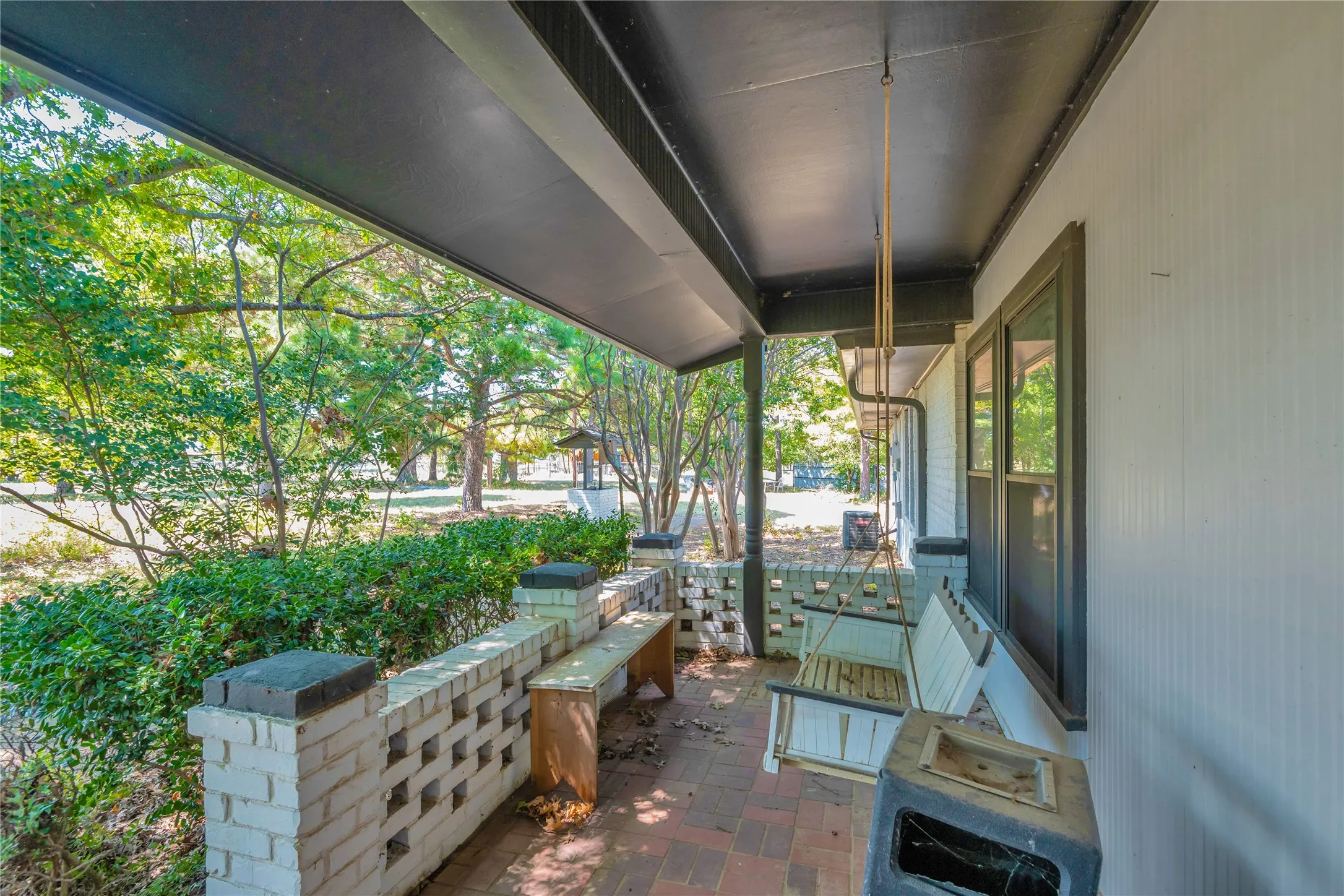 Covered porch with exposed brick flooring and white siding